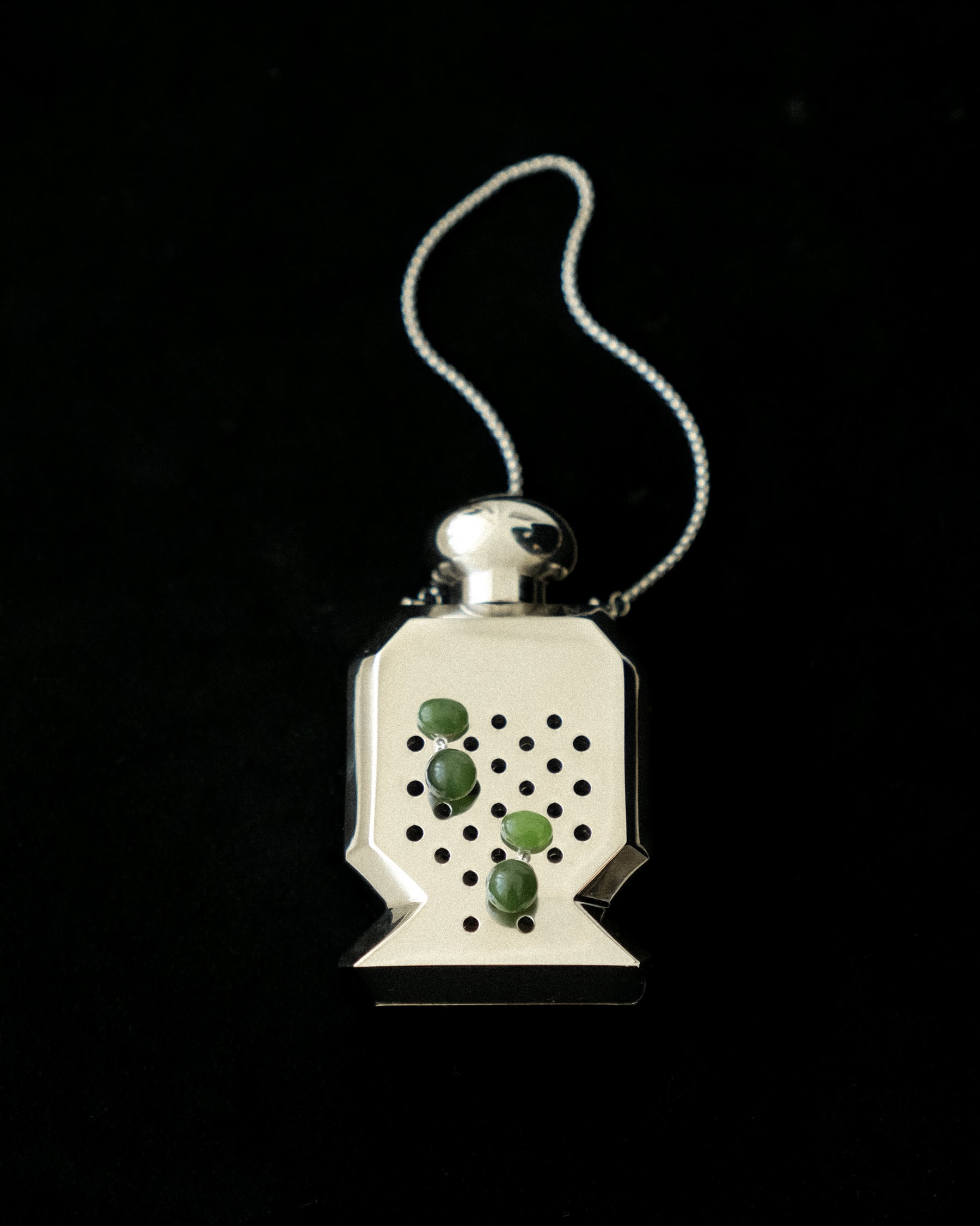 Tiny drop earrings in nephrite jade, set in a silver scented bottle, on a black background.