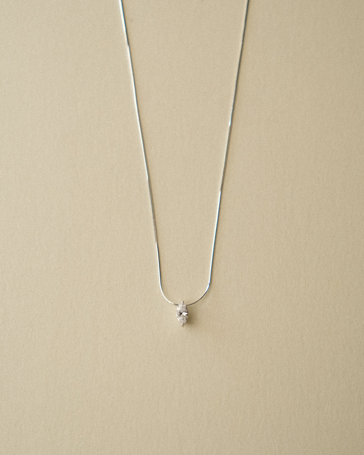 A close-up of a marquise diamond pendant necklace captured against a warm-toned wabi-sabi backdrop.