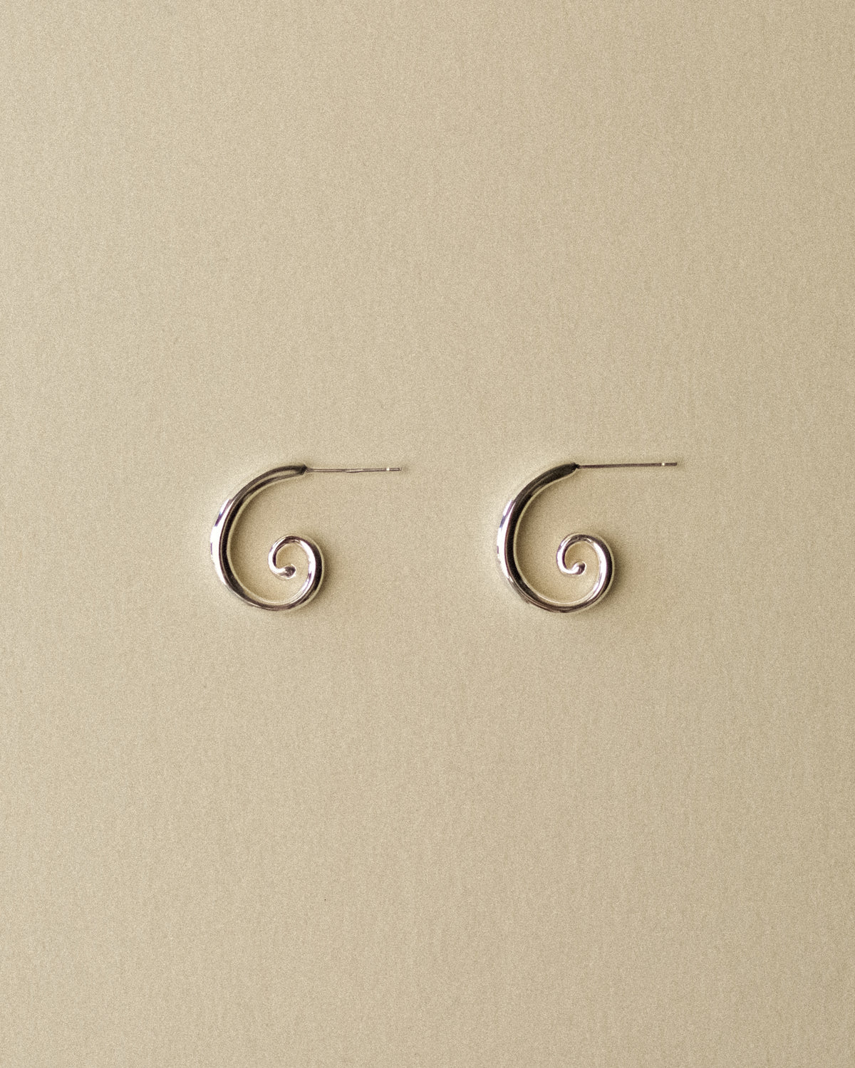A pair of Art Deco spiral stud earrings resting flat against a warm wabi-sabi backdrop, highlighting their sculptural curves and timeless form.