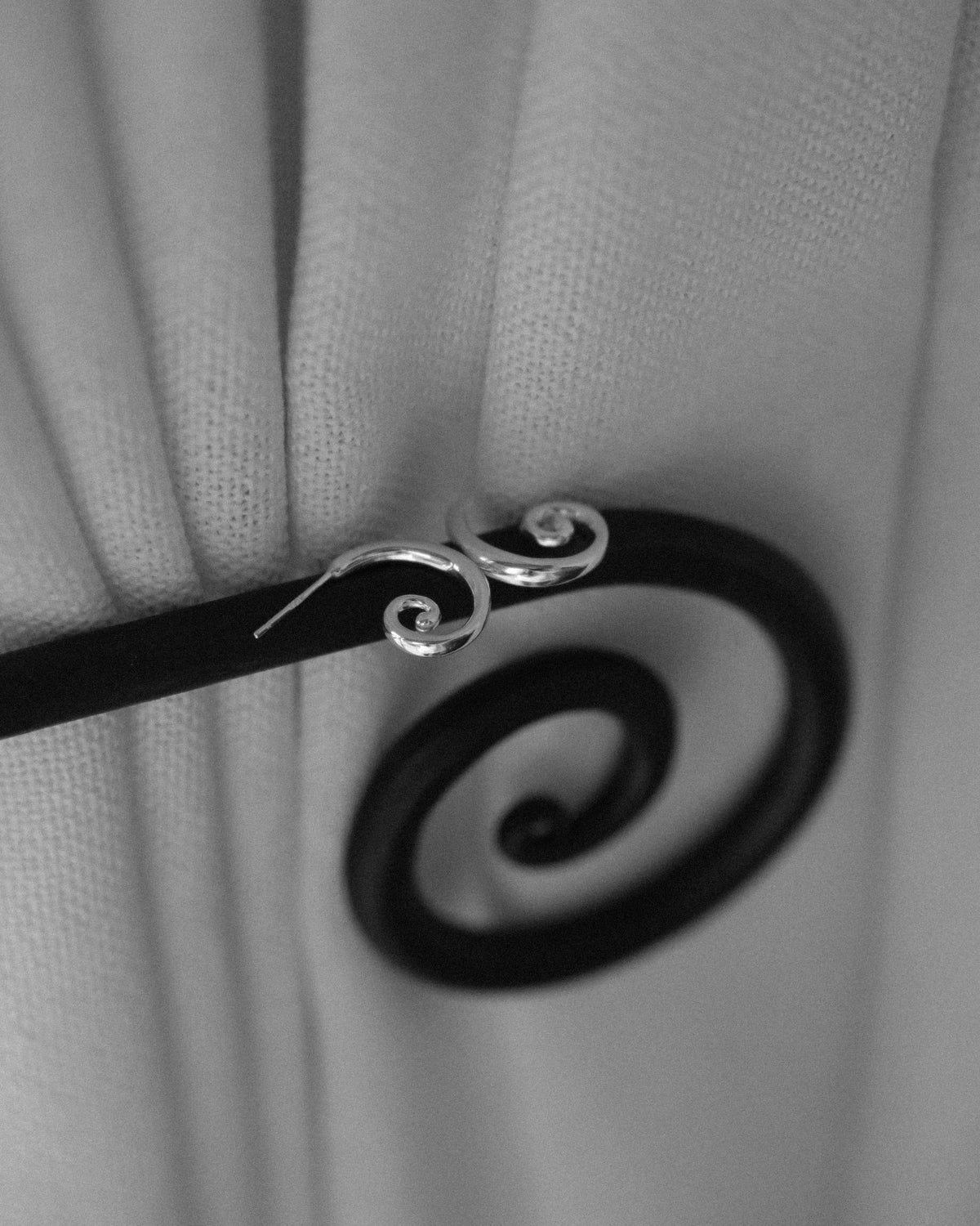 A pair of Art Deco inspired spiral stud earrings captured alongside a spiral handle in monochrome, echoing the sculptural curves and timeless elegance of the design.