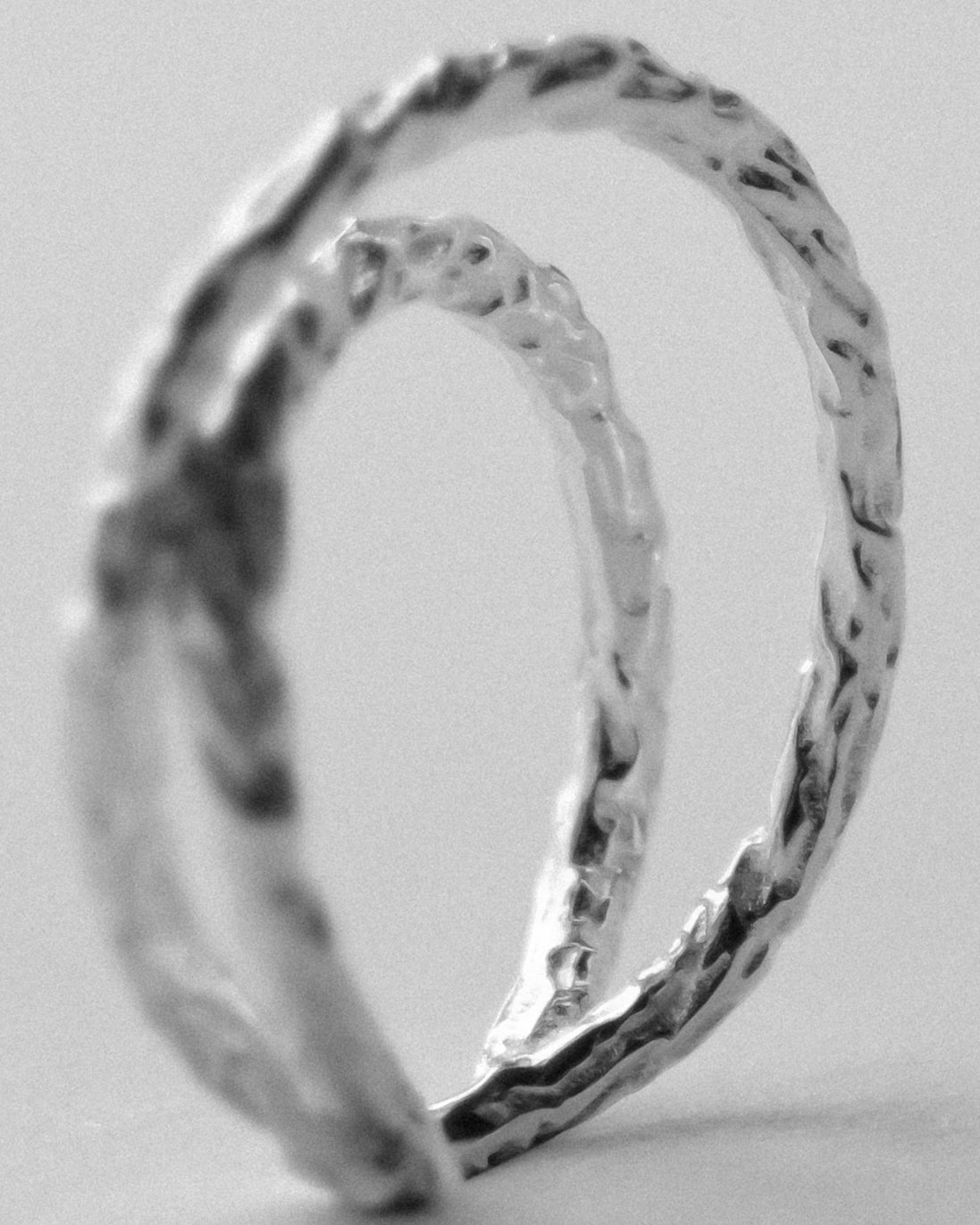 A close-up of a textured silver ring featuring a hammered design and organic surface finish, highlighting its architectural-inspired angles and sculptural details against a soft, neutral light background.
