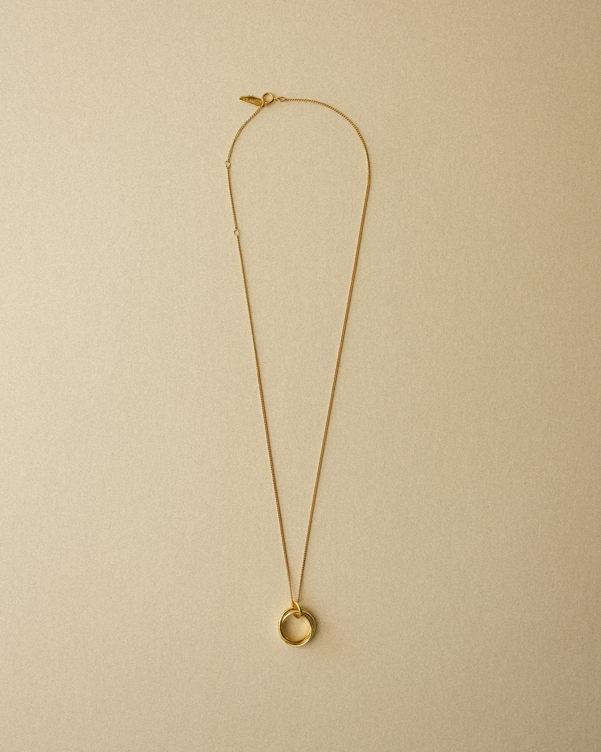 A gold Trio Interlink pendant necklace captured from above, revealing the full piece against a warm wabi-sabi backdrop that highlights its sculptural and timeless form.
