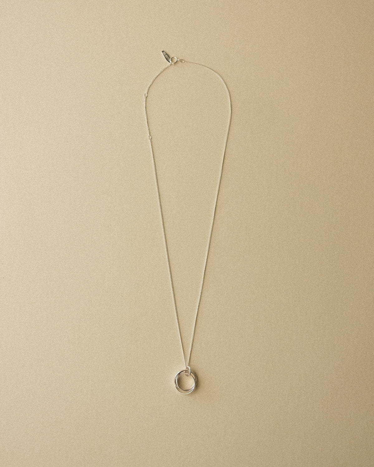 A silver Trio Interlink pendant necklace captured from above, revealing the full piece against a warm wabi-sabi backdrop that highlights its sculptural and timeless form.