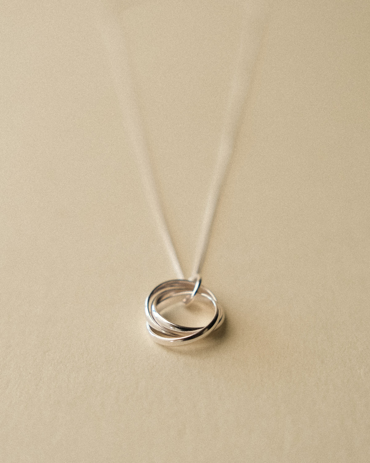 A silver Trio Interlink pendant necklace captured from the front, set against a warm wabi-sabi backdrop that highlights its sculptural and timeless form.