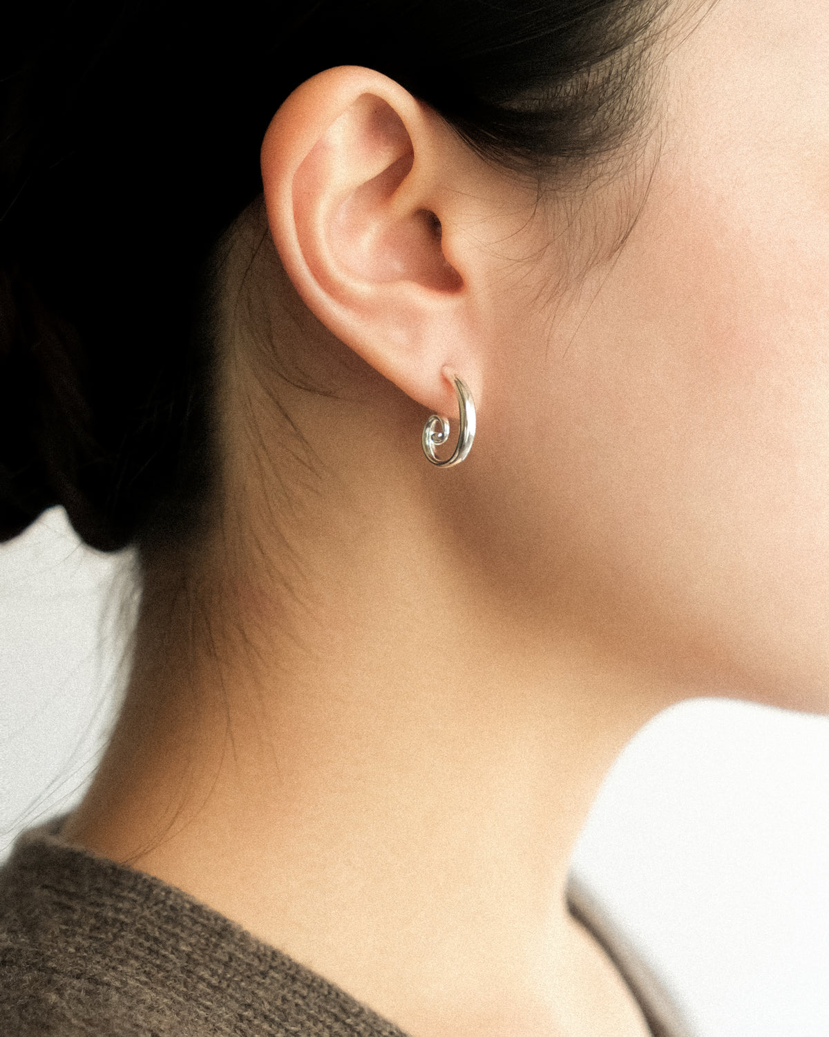 A close-up side profile of a woman wearing Art Deco spiral stud earrings, highlighting the sculptural spiral form against a clean white backdrop.