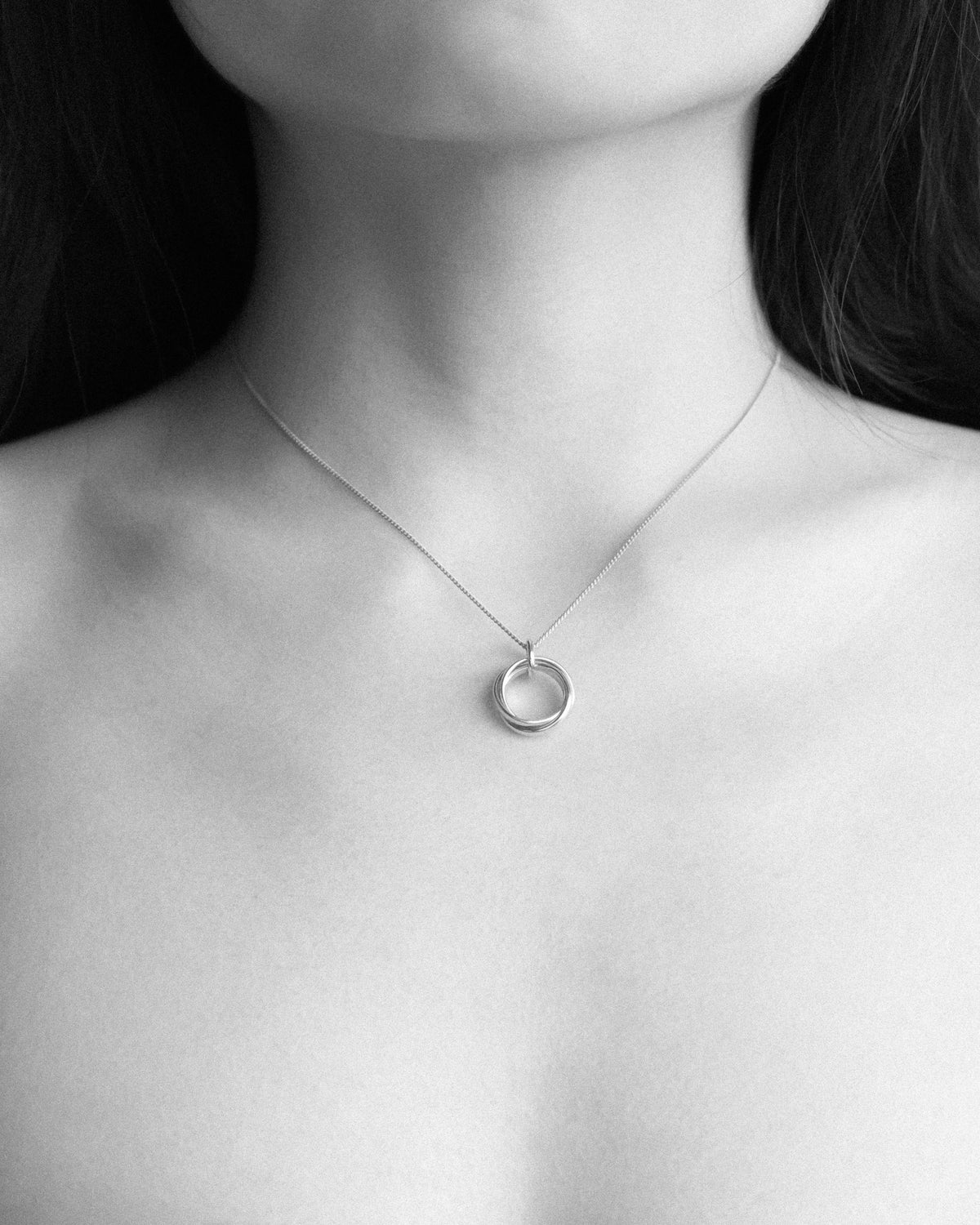 A close up monochrome of a woman adorned with the Trio Interlink pendant necklace, capturing its quiet and timeless elegance.