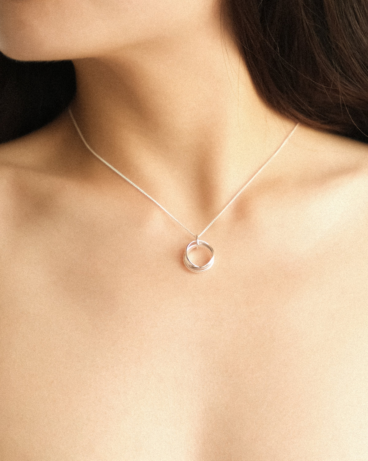 A close up of a woman adorned with the Trio Interlink pendant necklace in silver, capturing its quiet and timeless elegance.