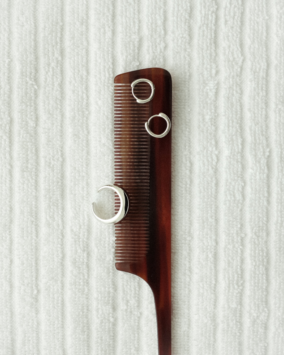 An acetate comb styled alongside silver earrings and a silver plated brass open pinky ring, placed softly on a white bath towel.