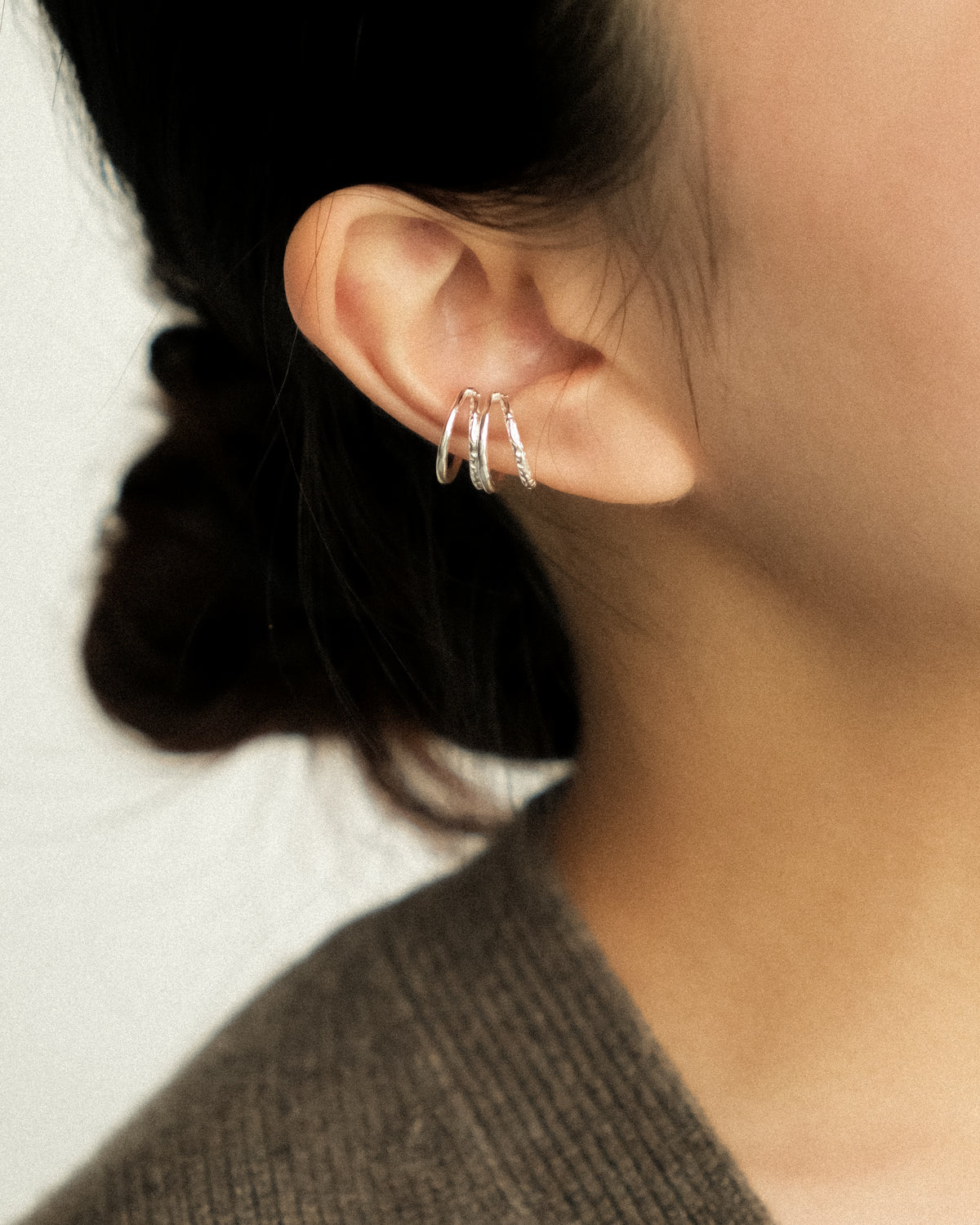 A pair of silver ear cuffs embracing the ear with a double-layered design, balancing the raw texture of hand-hammered silver with the refined sheen of a polished finish, set against a clean white background.