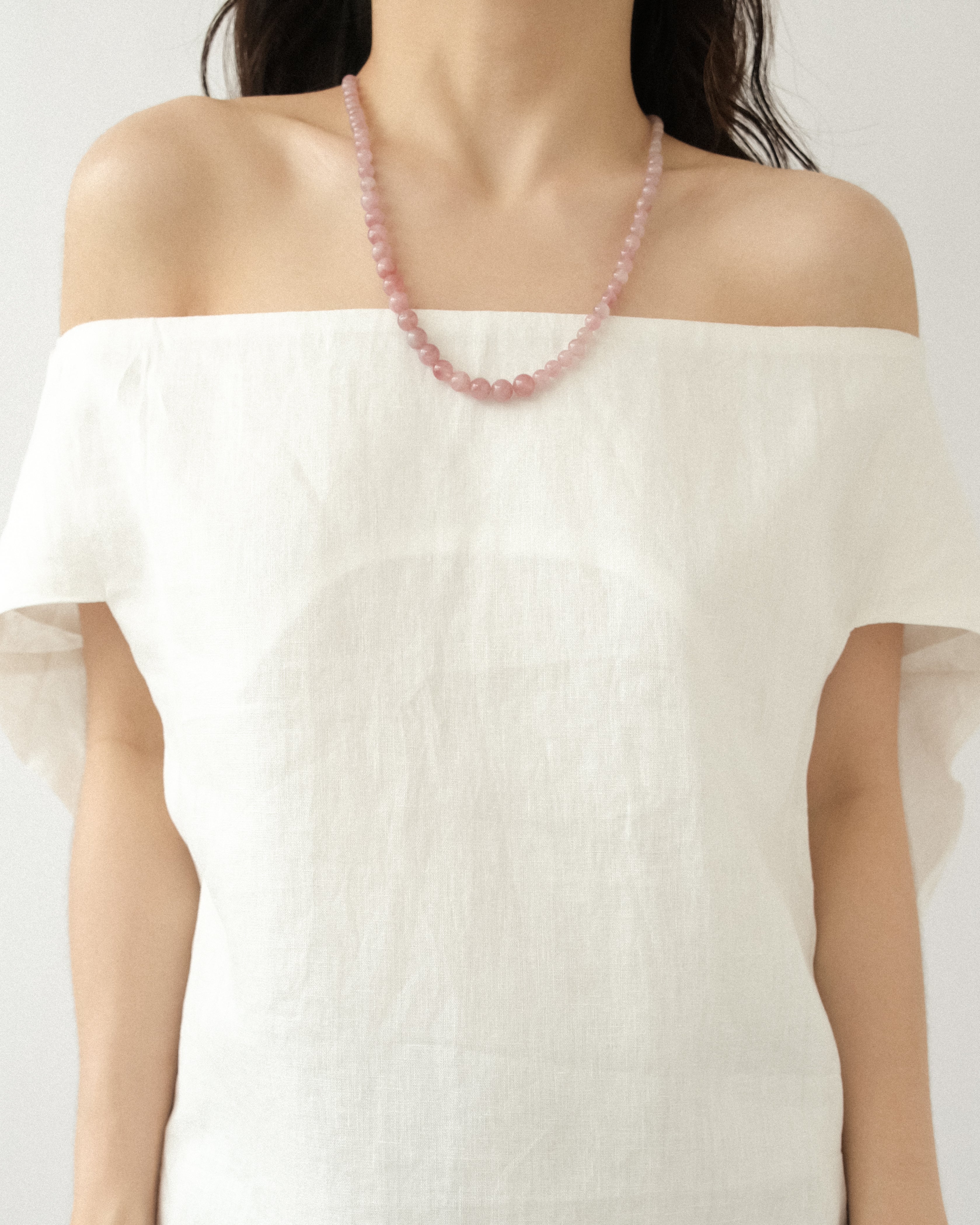 Person wearing a white off-shoulder top with a natural rose quartz necklace on a plain background