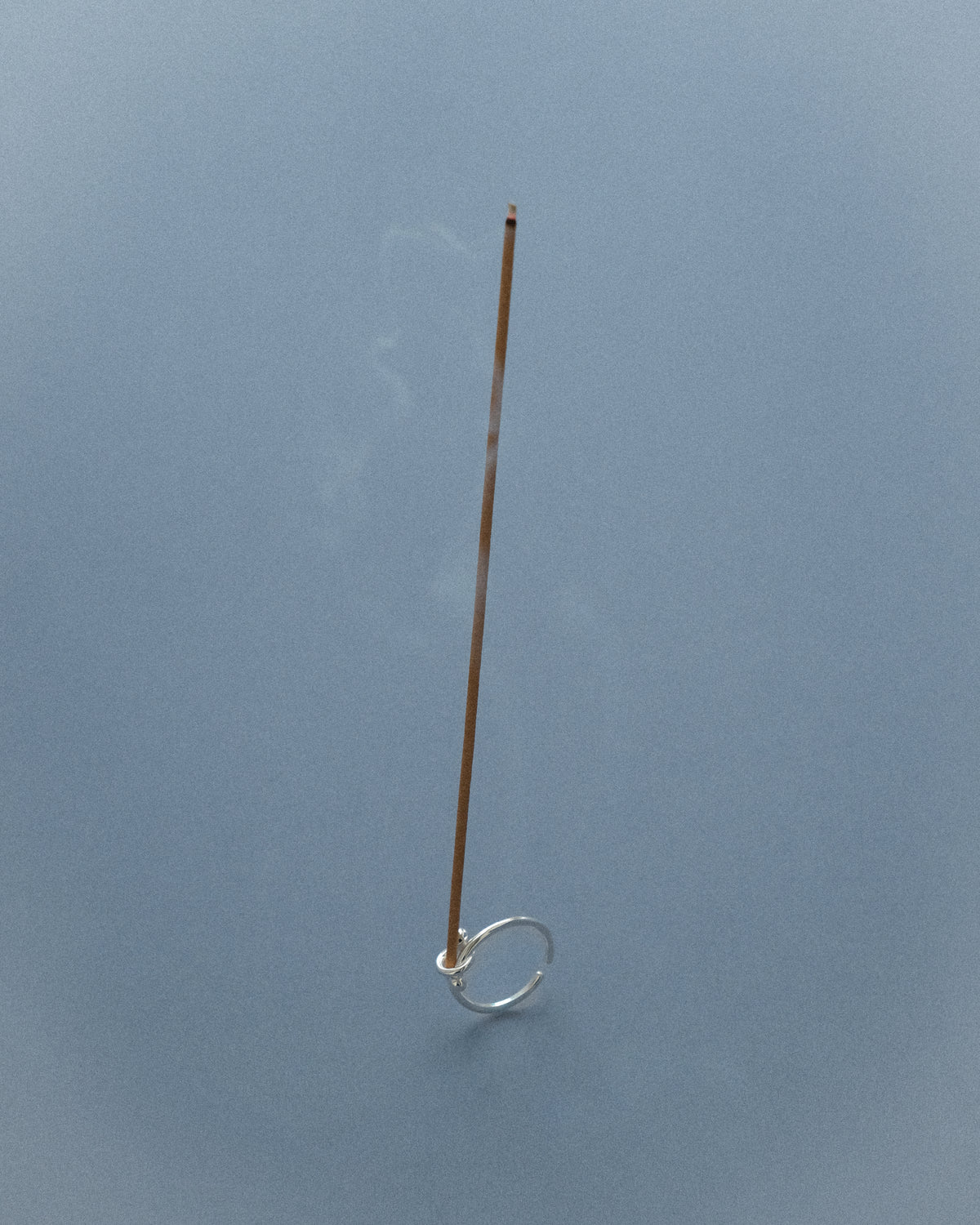 A knot design ring paired with an incense set as a prop, captured against a grey-blue background in a creative composition.