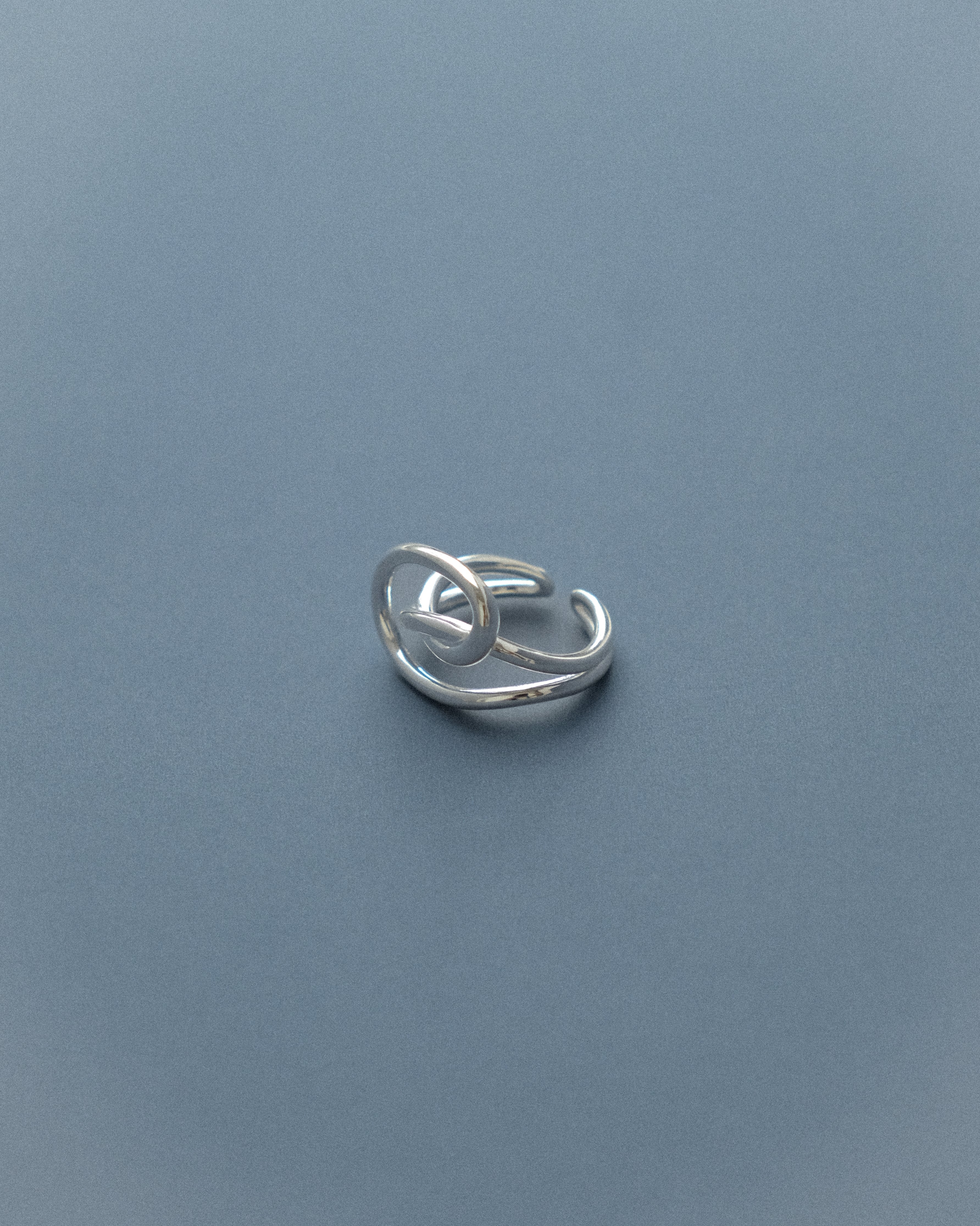 A line sculpture ring set against a serene blue background.