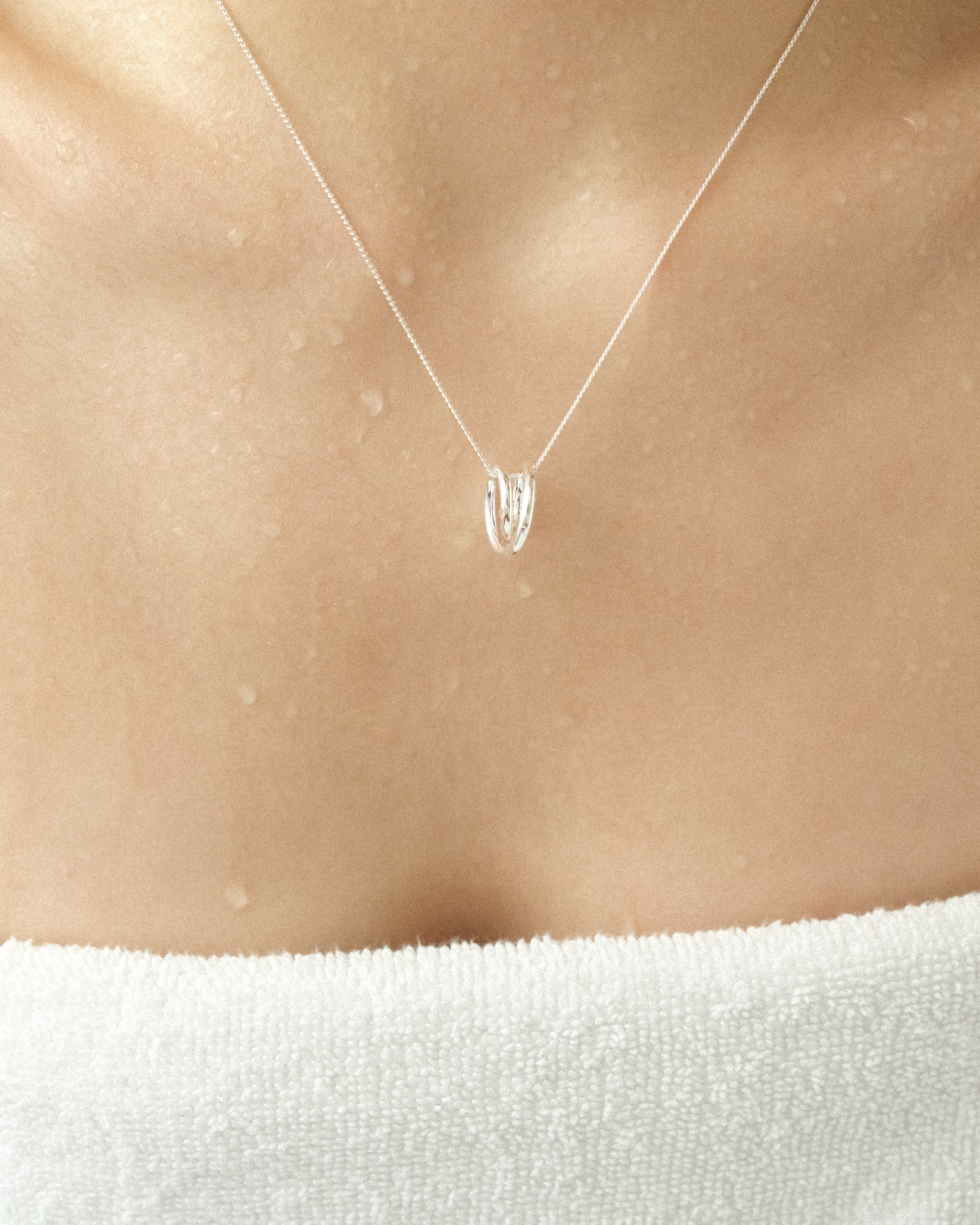 A silver line sculpture pendant necklace worn by a person wrapped in a bath towel.