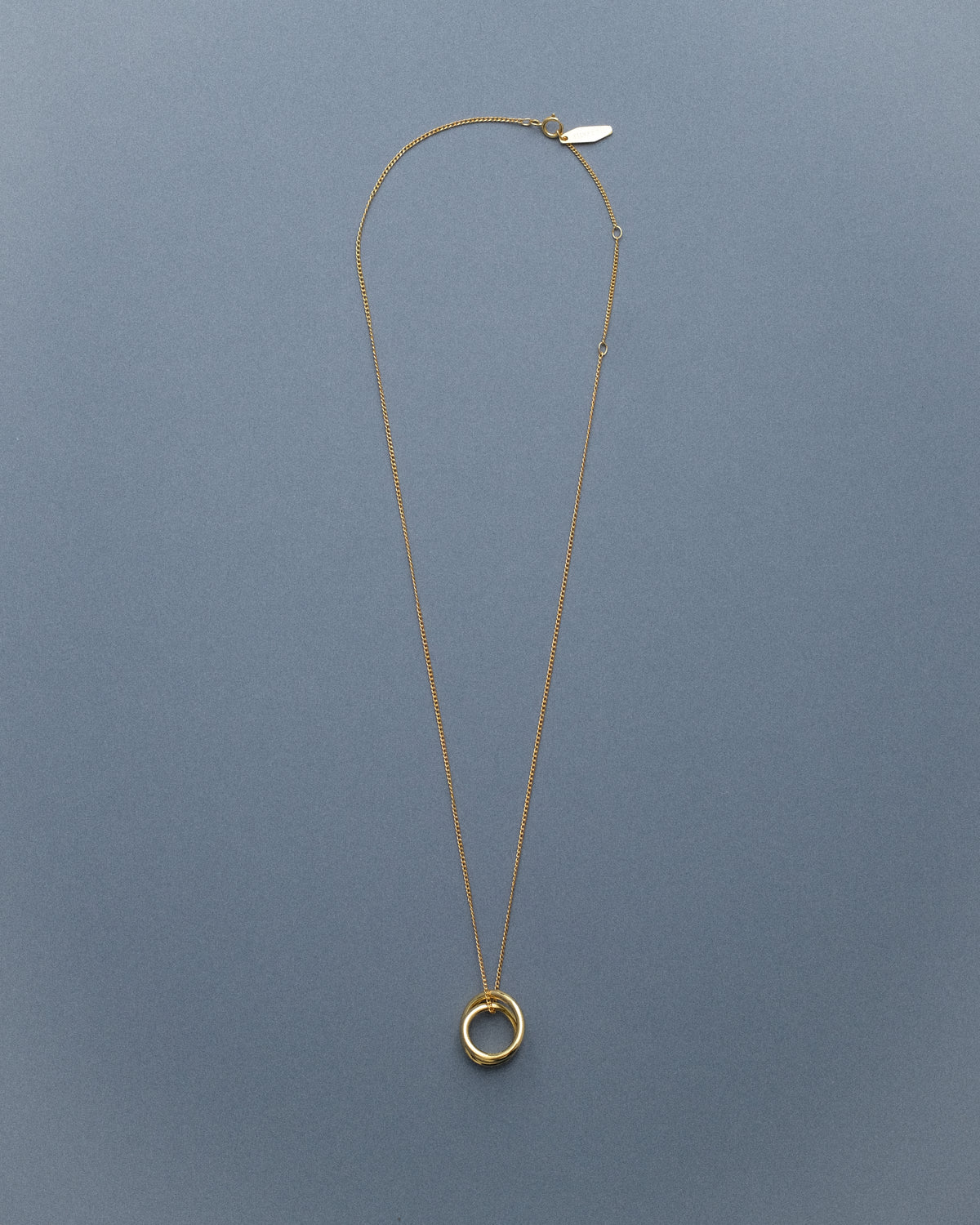 A gold line sculpture pendant necklace against a blue backdrop.