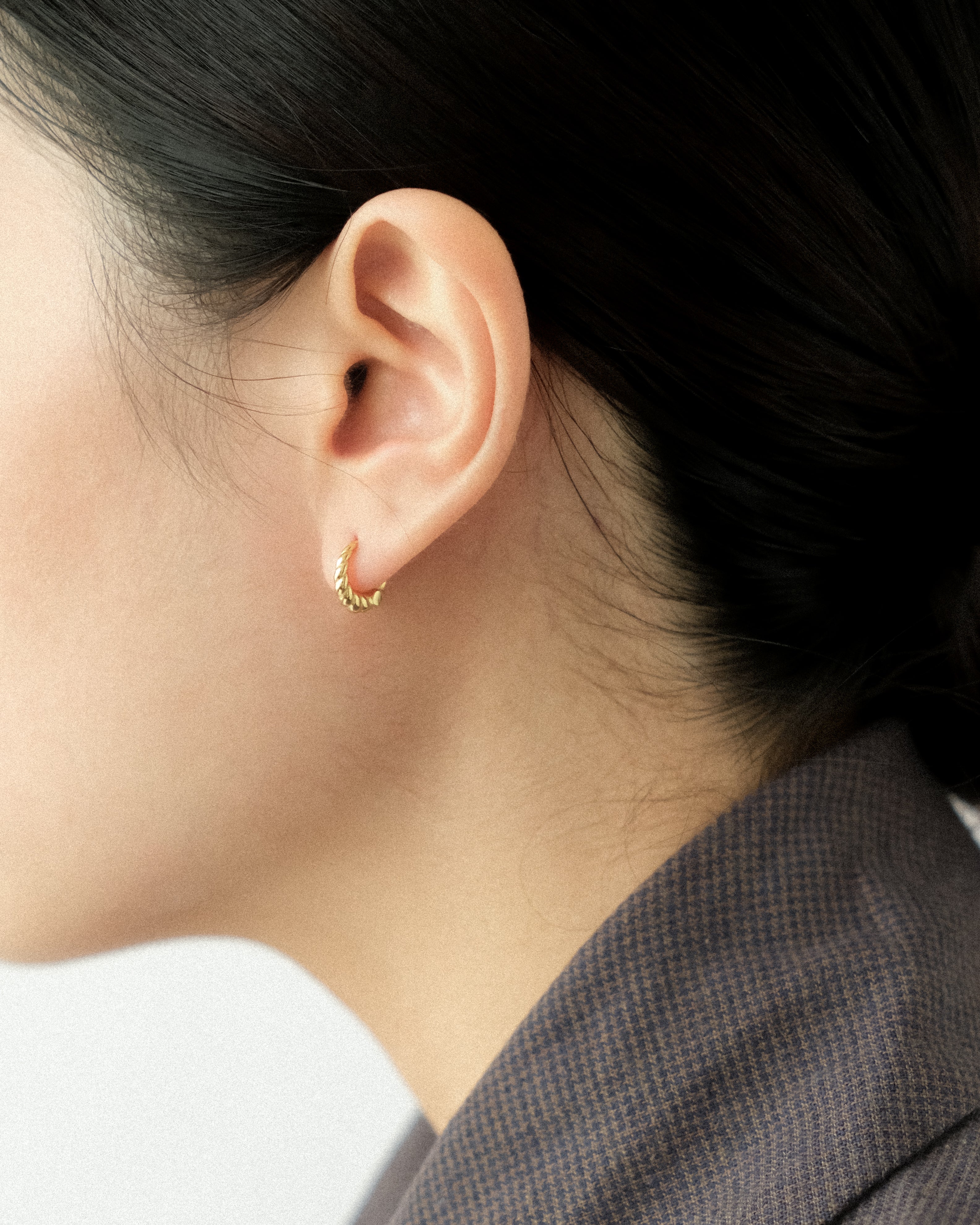 Close-up of an ear wearing a gold hoop earring with a blurred background.