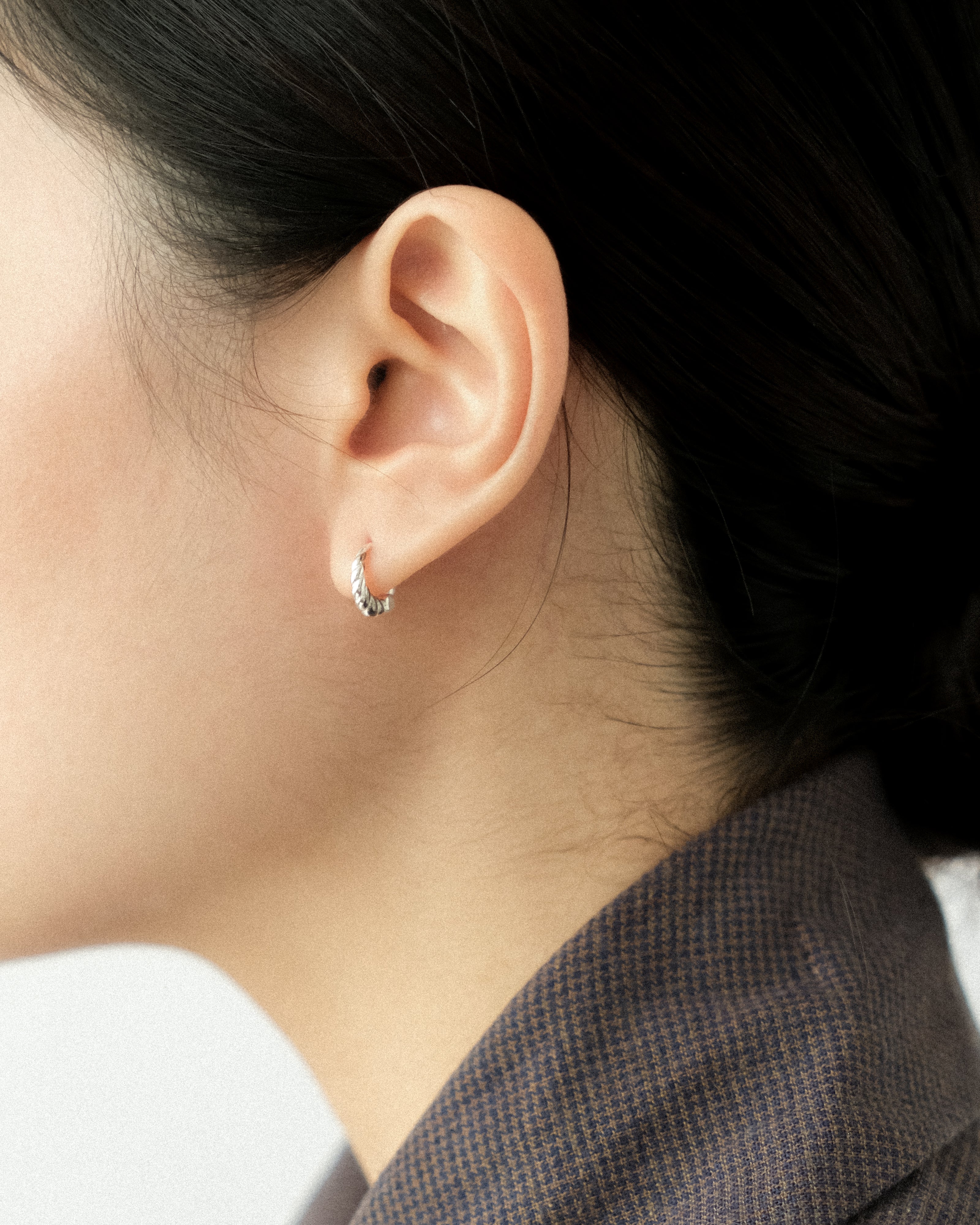 Close-up of an ear wearing a small silver hoop earring with a blurred background.
