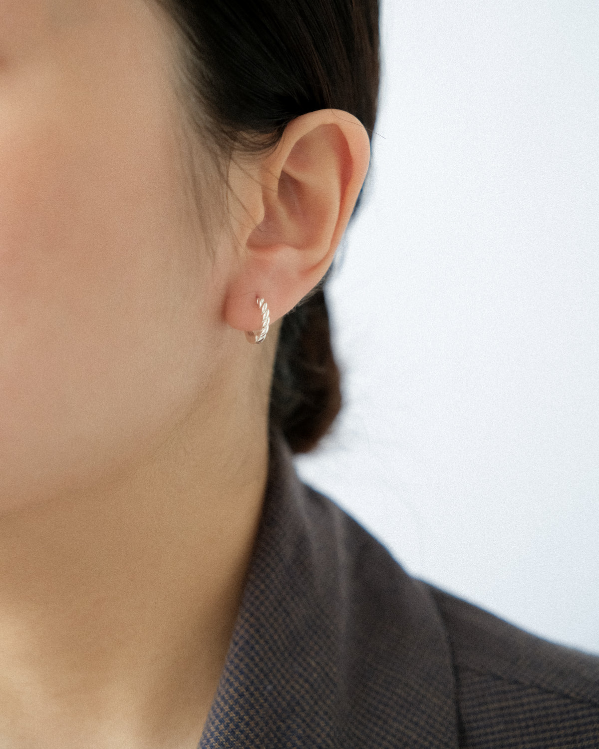 Close-up of an ear wearing a small spiral side earring with a blurred background