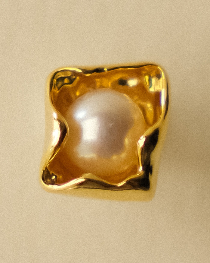 A close-up of a gold earring highlighting its geometric petal shape and central freshwater pearl.