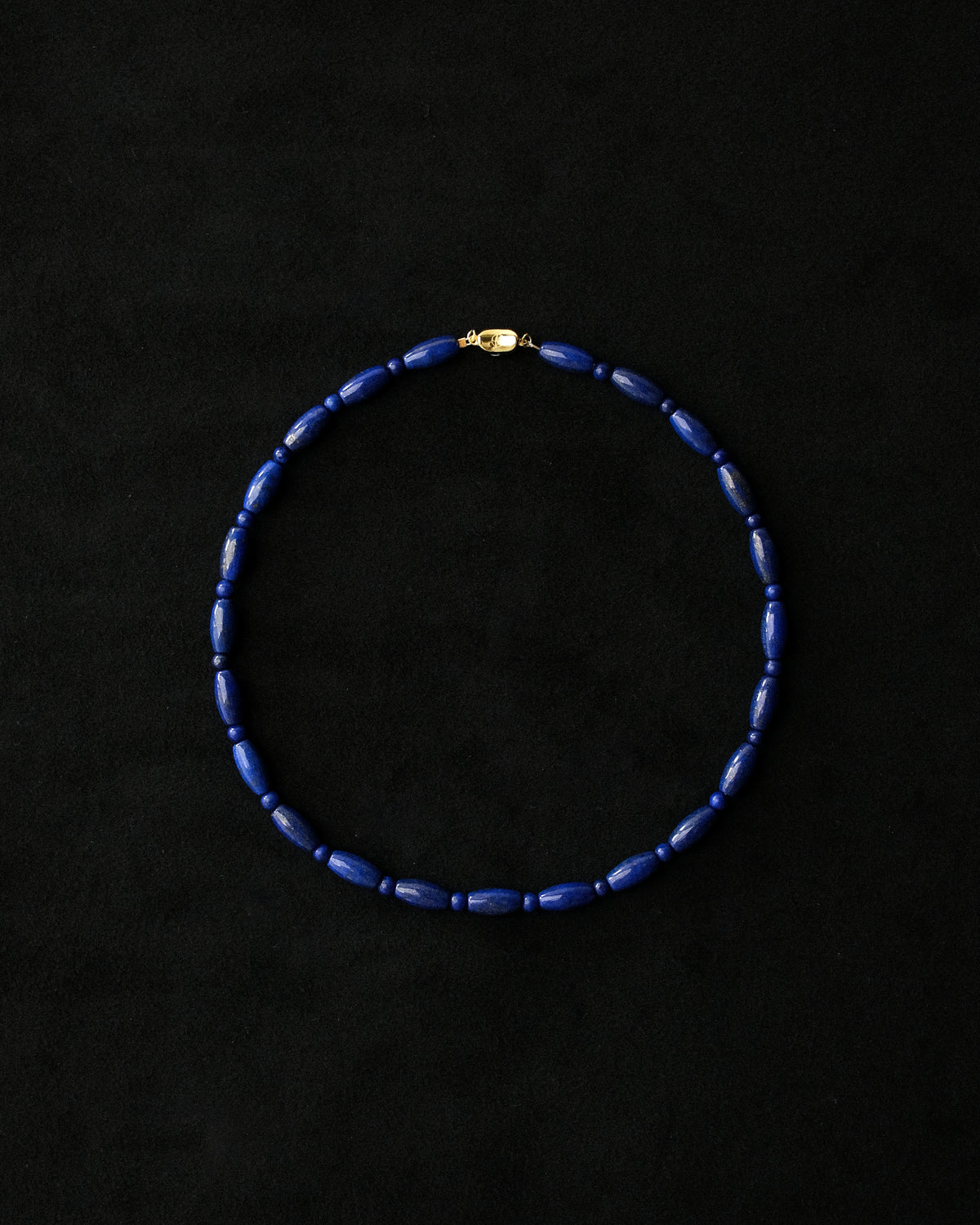 A beaded choker or collar made of dark blue lapis beads with a small gold clasp, displayed against a black background.