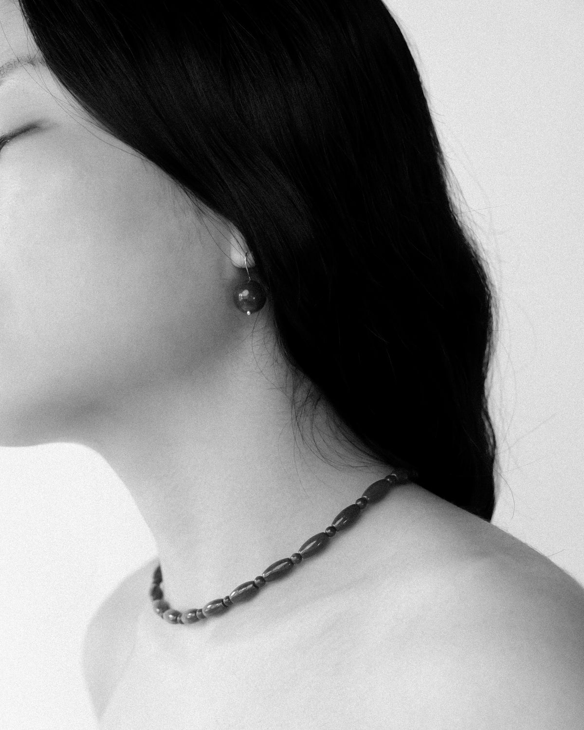 A woman wearing round stone earrings with a matching choker, elegantly styled in black and white photography.