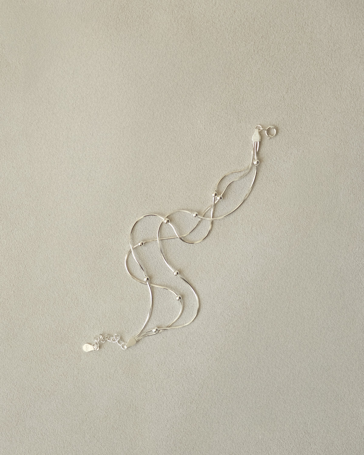 Trio of silver snake chain bracelets, accented with silver balls captured with a beige background.