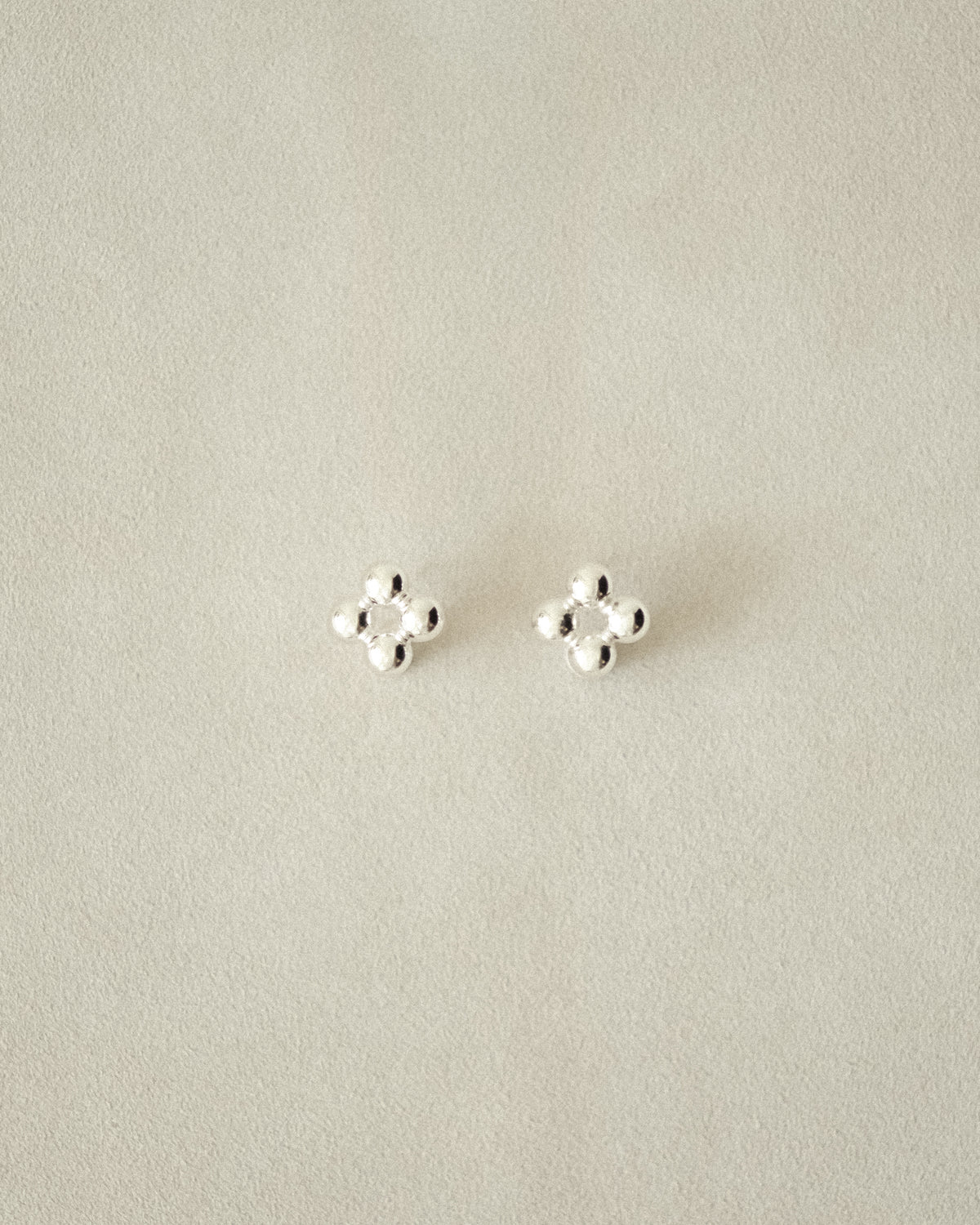 Flower-shaped silver beaded earrings, set against a beige background.