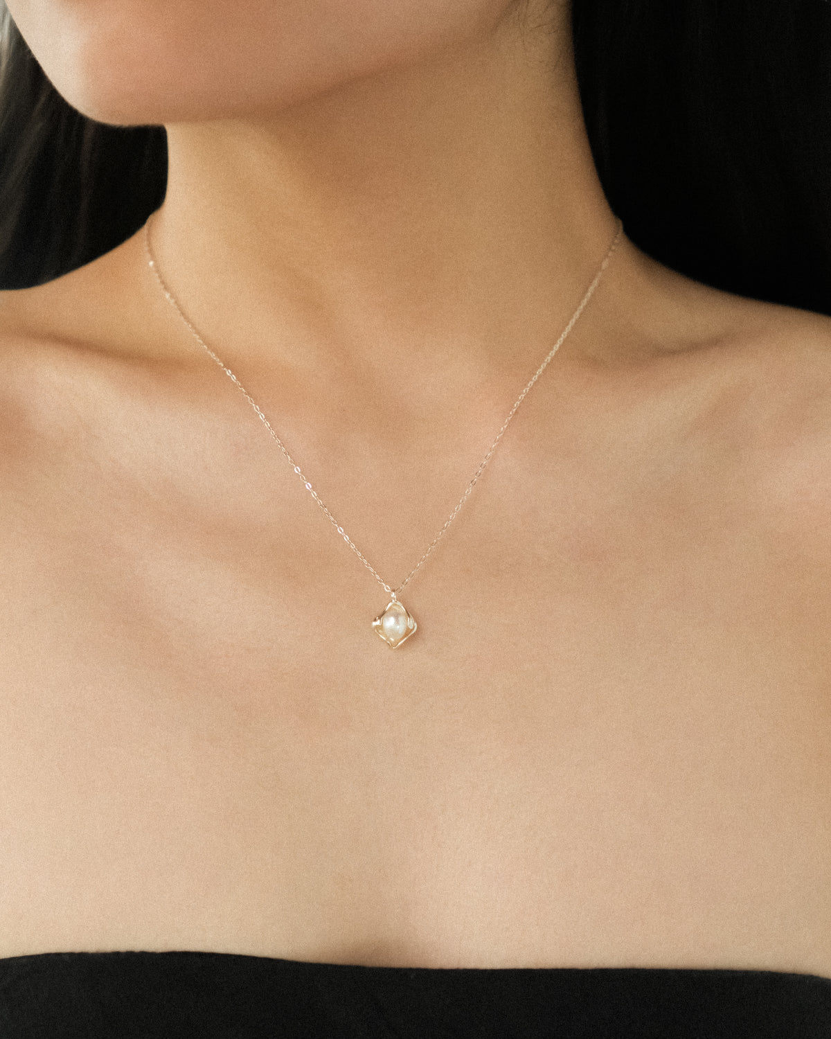 A delicate silver chain necklace with a petal-shaped, textured silver pendant featuring a central white freshwater pearl, shown worn around a model’s neck.