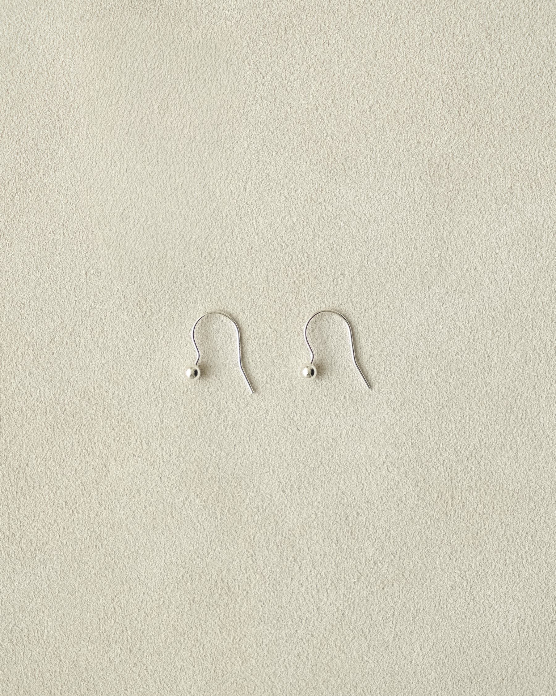 Pair of tiny silver dangle ball earrings on a beige background