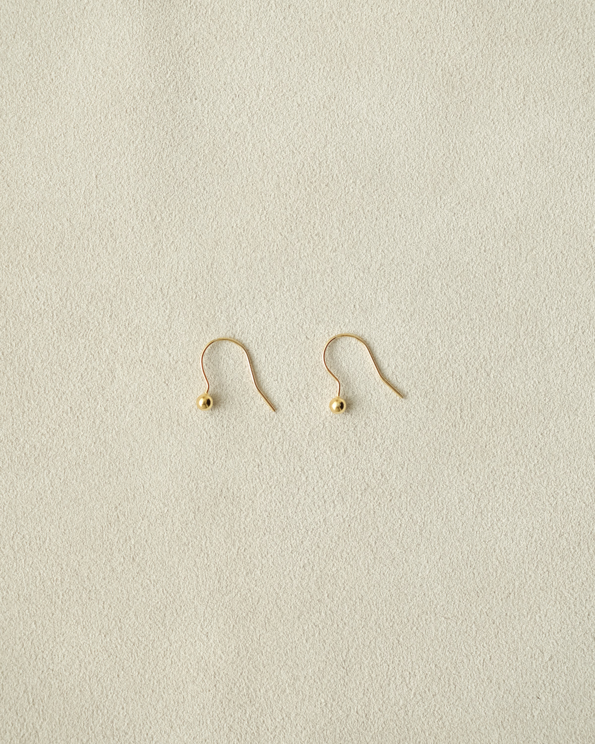 Pair of tiny gold dangle ball earrings on a beige background