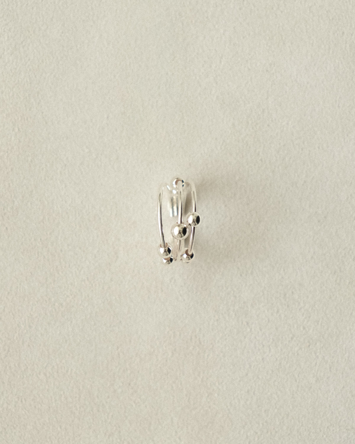 The second shot of a trio of silver rings with silver ball accents, arranged to mimic the gentle movement of the beads, set against a beige background