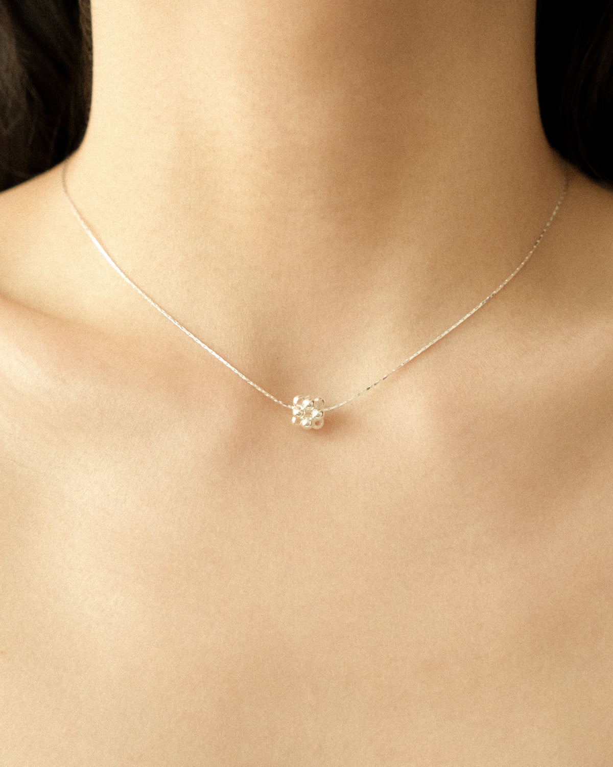 A silver necklace featuring a delicate ball-beaded pendant, styled on the neck like a choker.