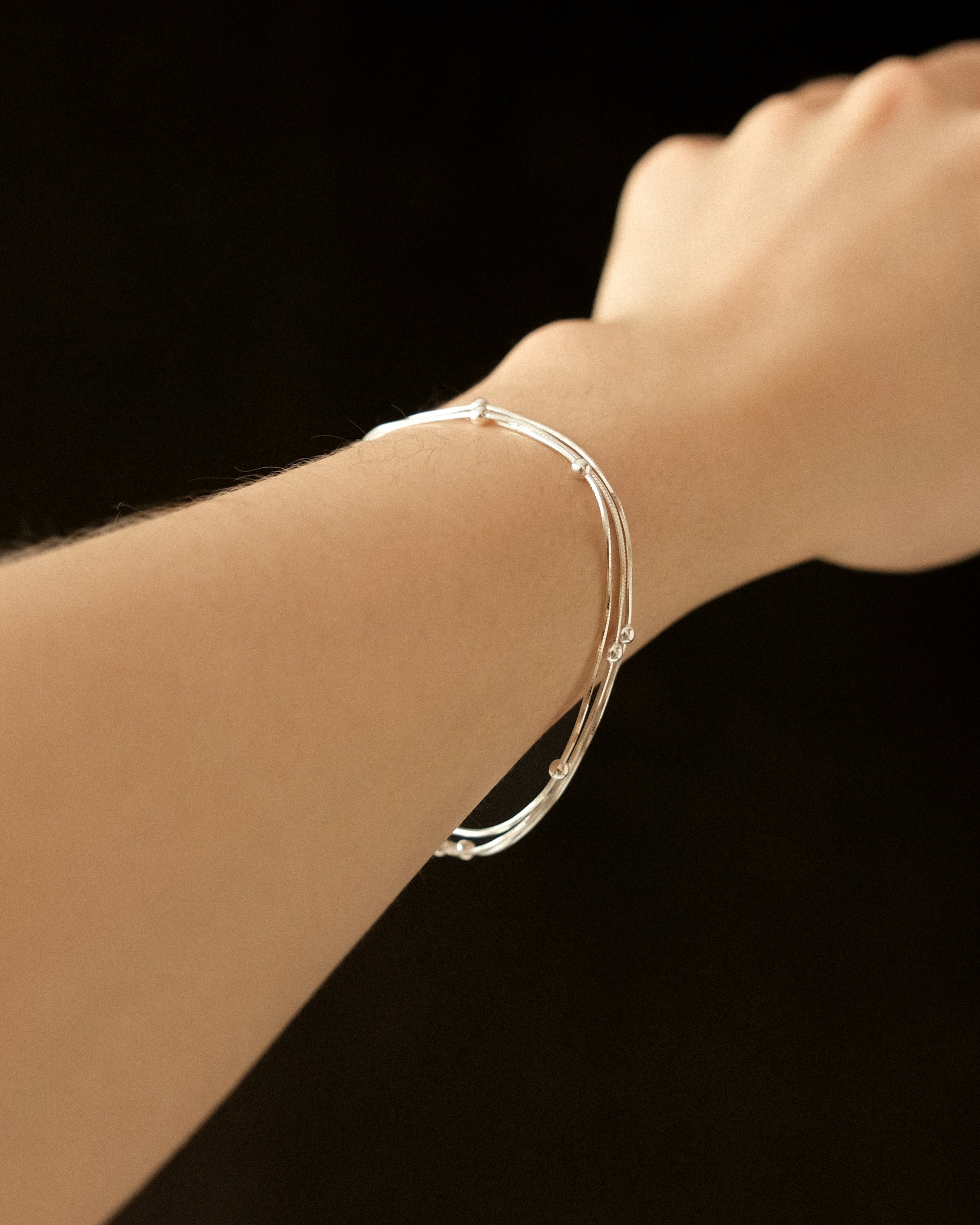 Trio of silver snake chain bracelets, accented with silver balls, worn on a wrist against a black background.