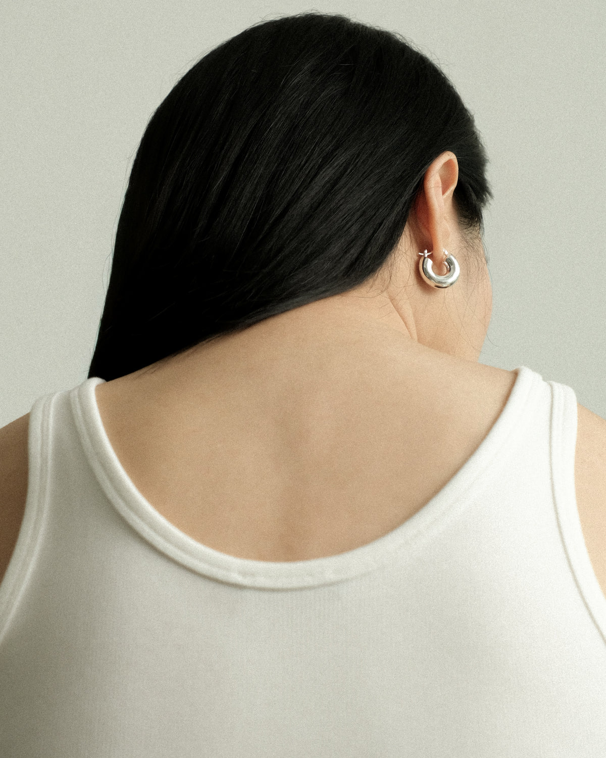 Person wearing a silver hoop earring with a neutral background
