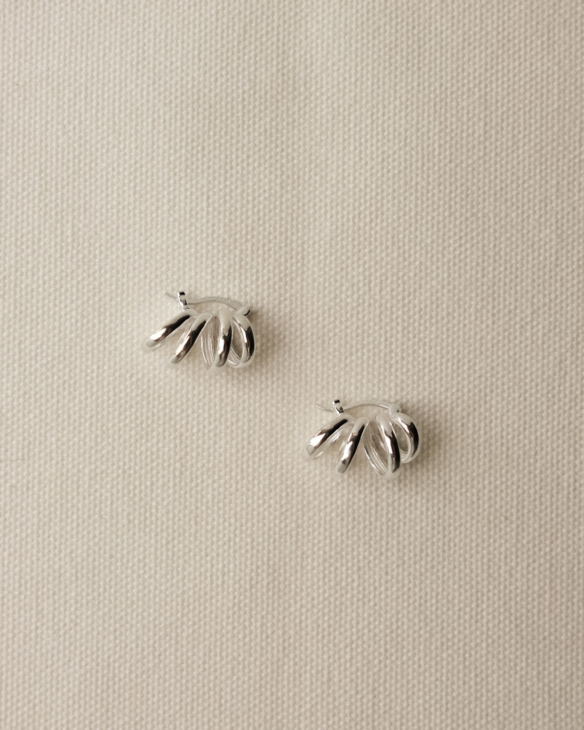 A pair of silver-toned twisting hoop earrings displayed on a textured beige tablecloth background.