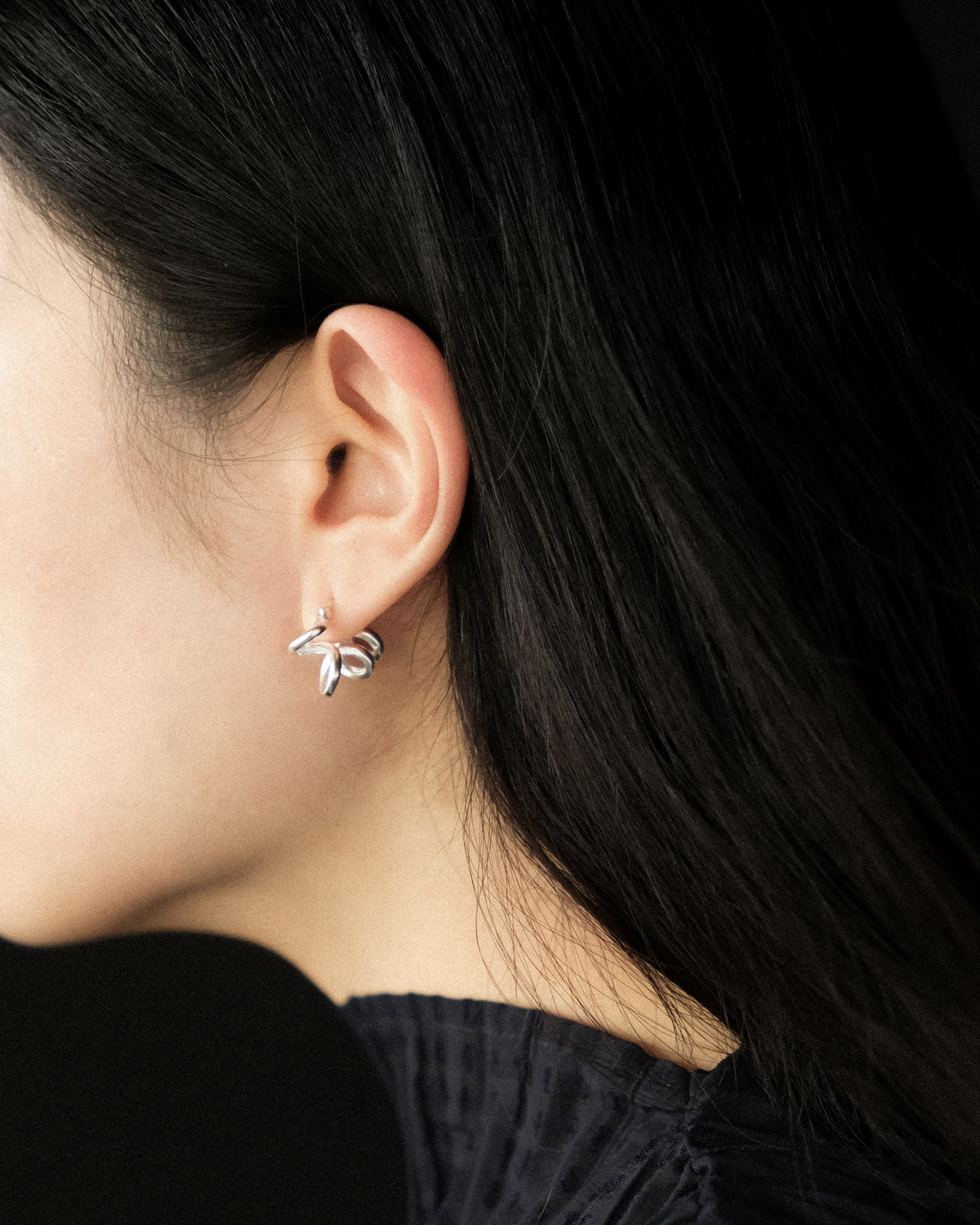 Close up of a model wearing sculptural brushed sterling silver hoop earring with curved loops.