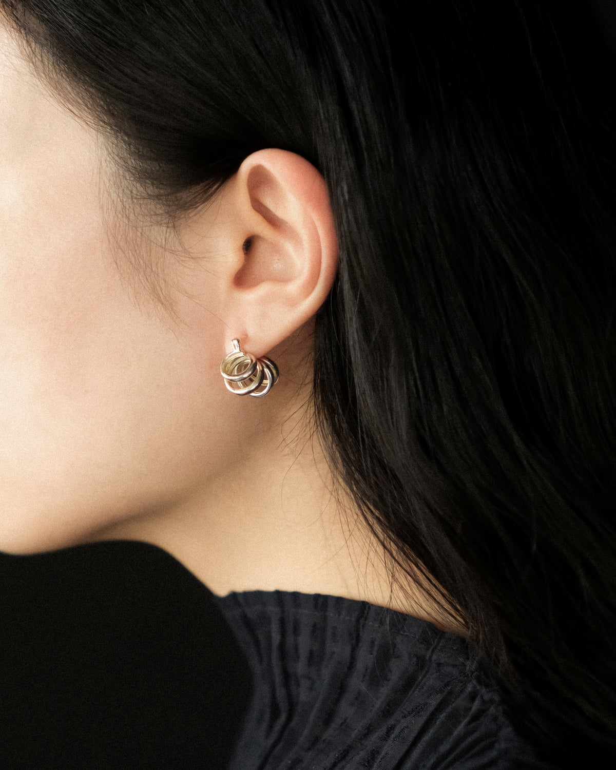 A close-up side profile of a woman with dark hair wearing a silver hoop earring with twisting hoops.