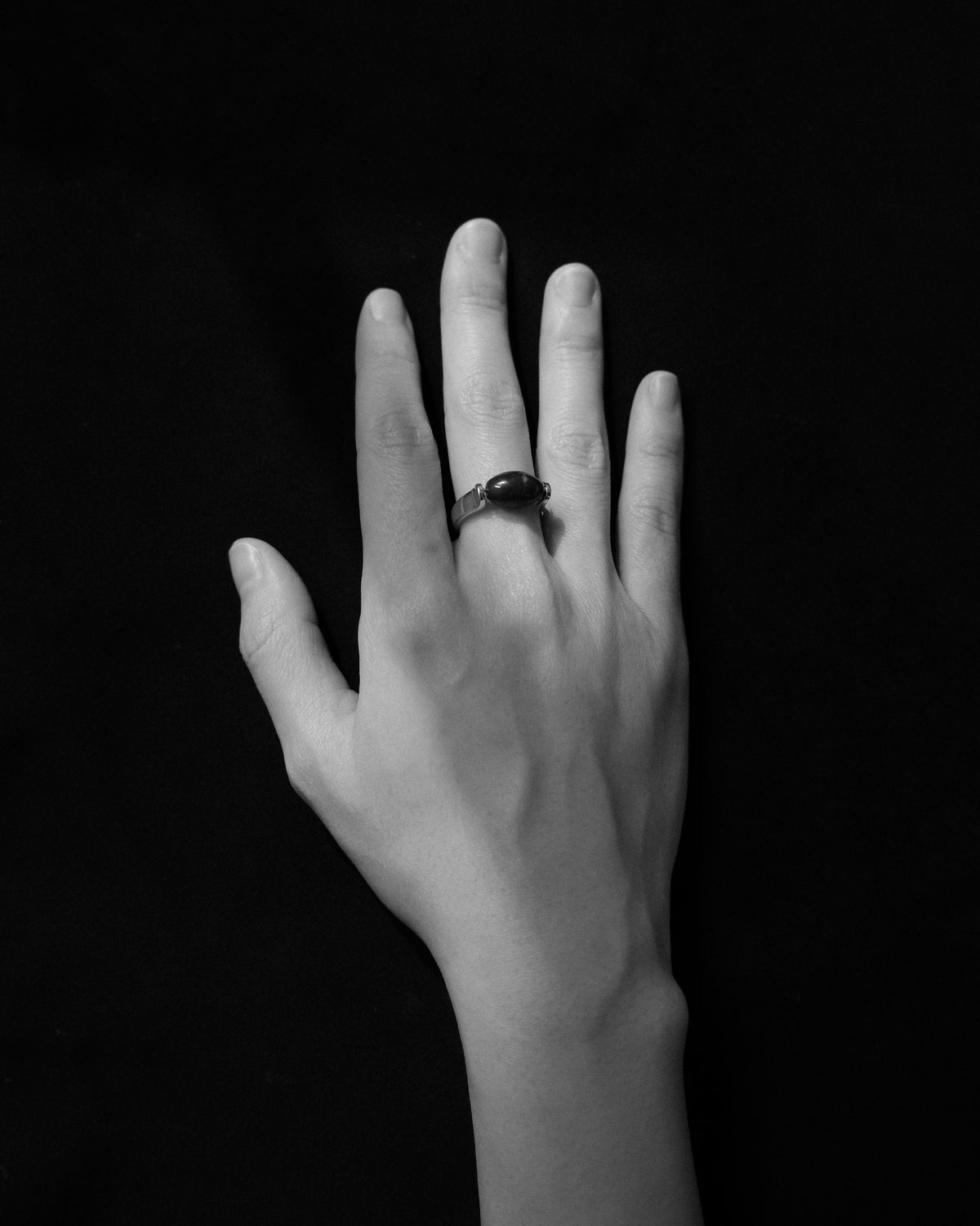 Black and white close up of a hand wearing a sculptural silver ring set with an oval lapis lazuli stone against a dark background.