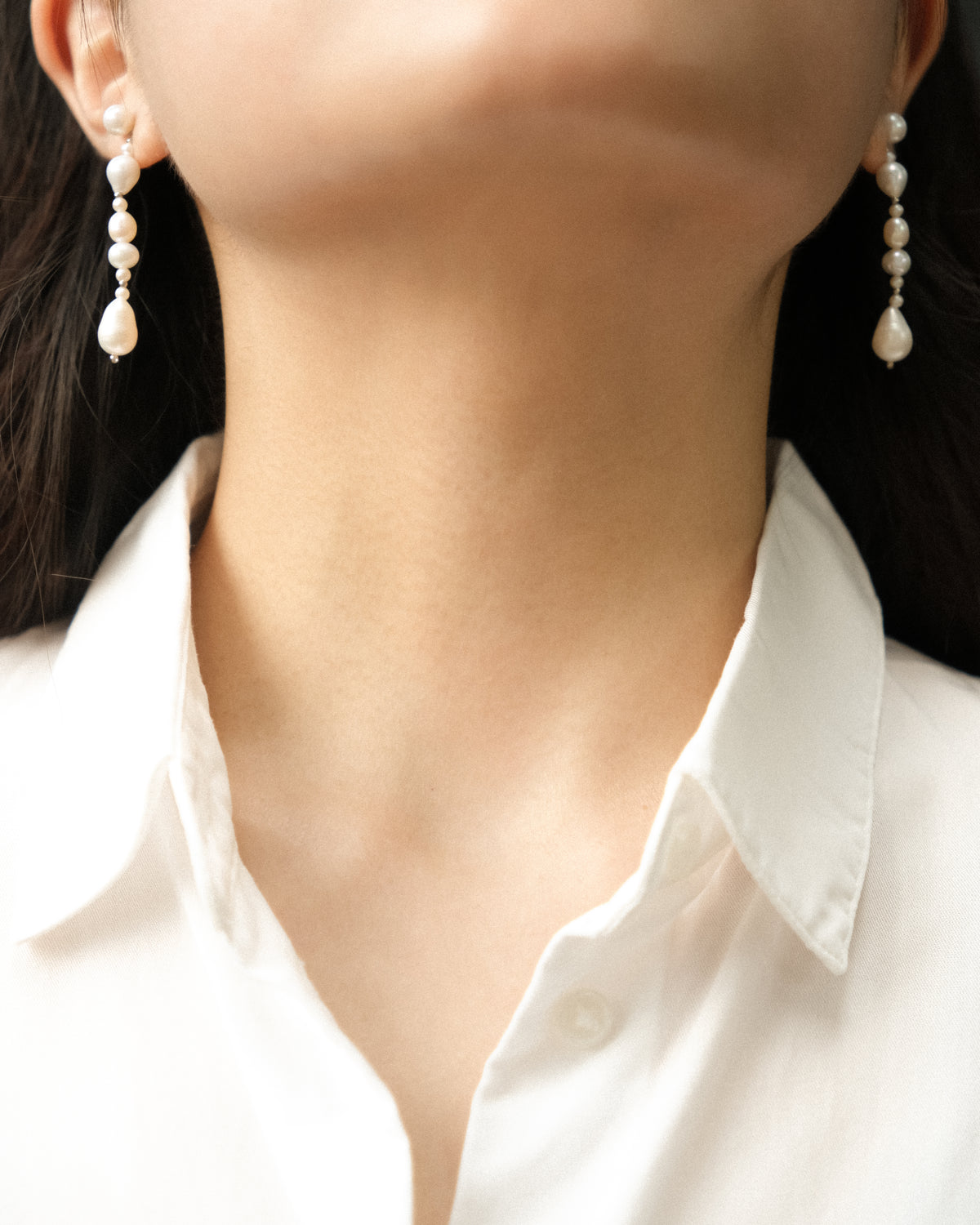 Long pearl earrings worn by a person with a white shirt