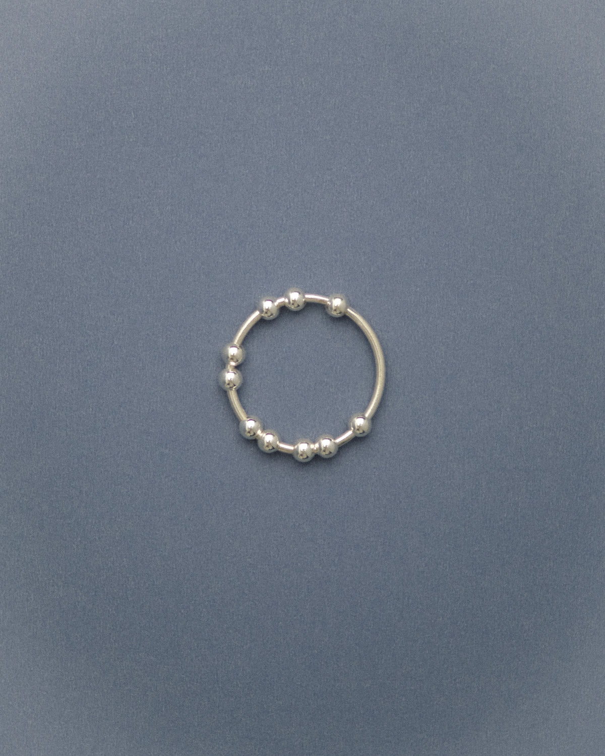 Silver flowing bead ring on a grey-blue background