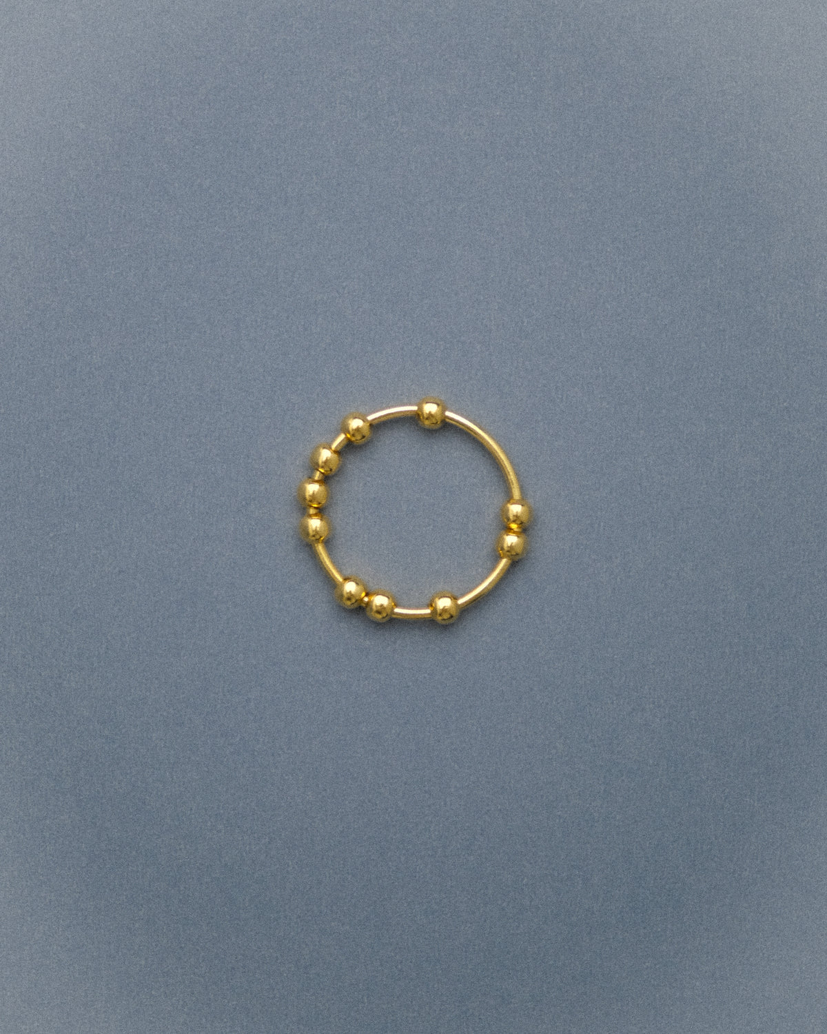 Gold flowing bead ring on a grey-blue background