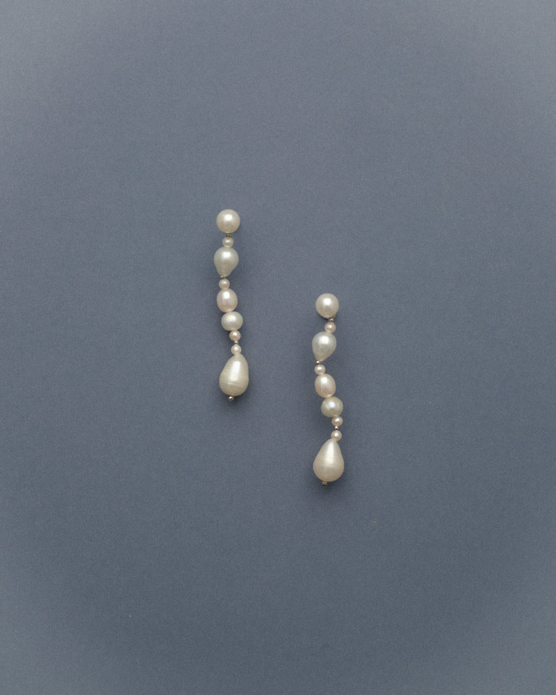 Pair of long pearl earrings on a grey blue background