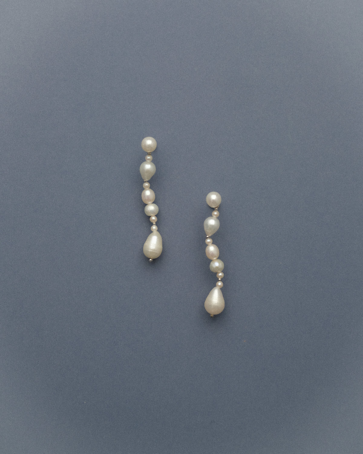 Pair of long pearl earrings on a grey blue background