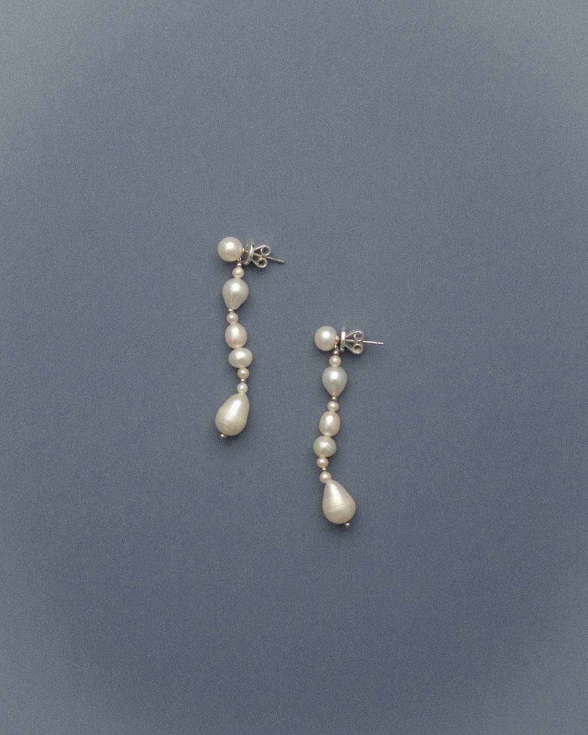 Pair of long pearl earrings on a grey blue background