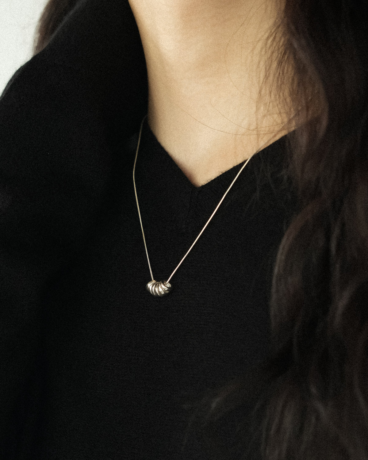 A close-up of a person wearing a delicate gold chain necklace with a cluster of round silver pendants, styled with a black V-neck cashmere sweater.