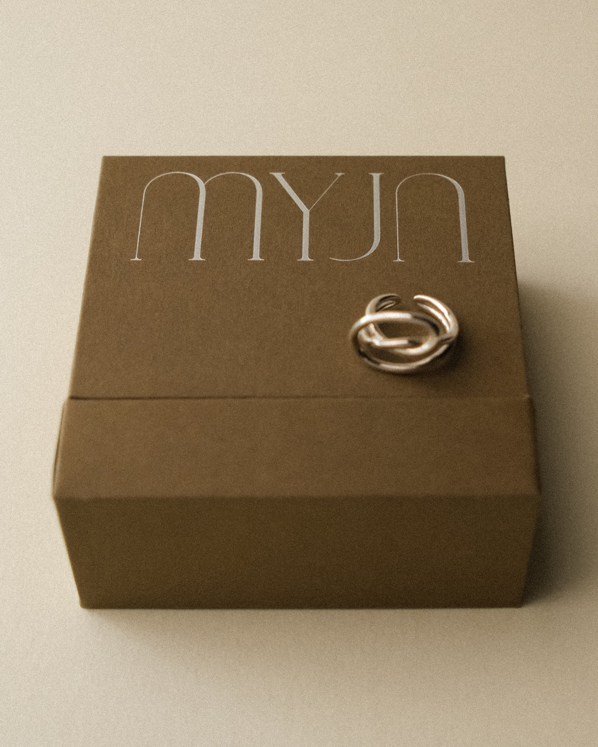 A light khaki brown jewellery box crafted from the skin and shell of hazelnuts, set against a warm wabi sabi backdrop. Paired with the Cosette Sculptural Ring, the composition celebrates quiet materiality and sculptural form.