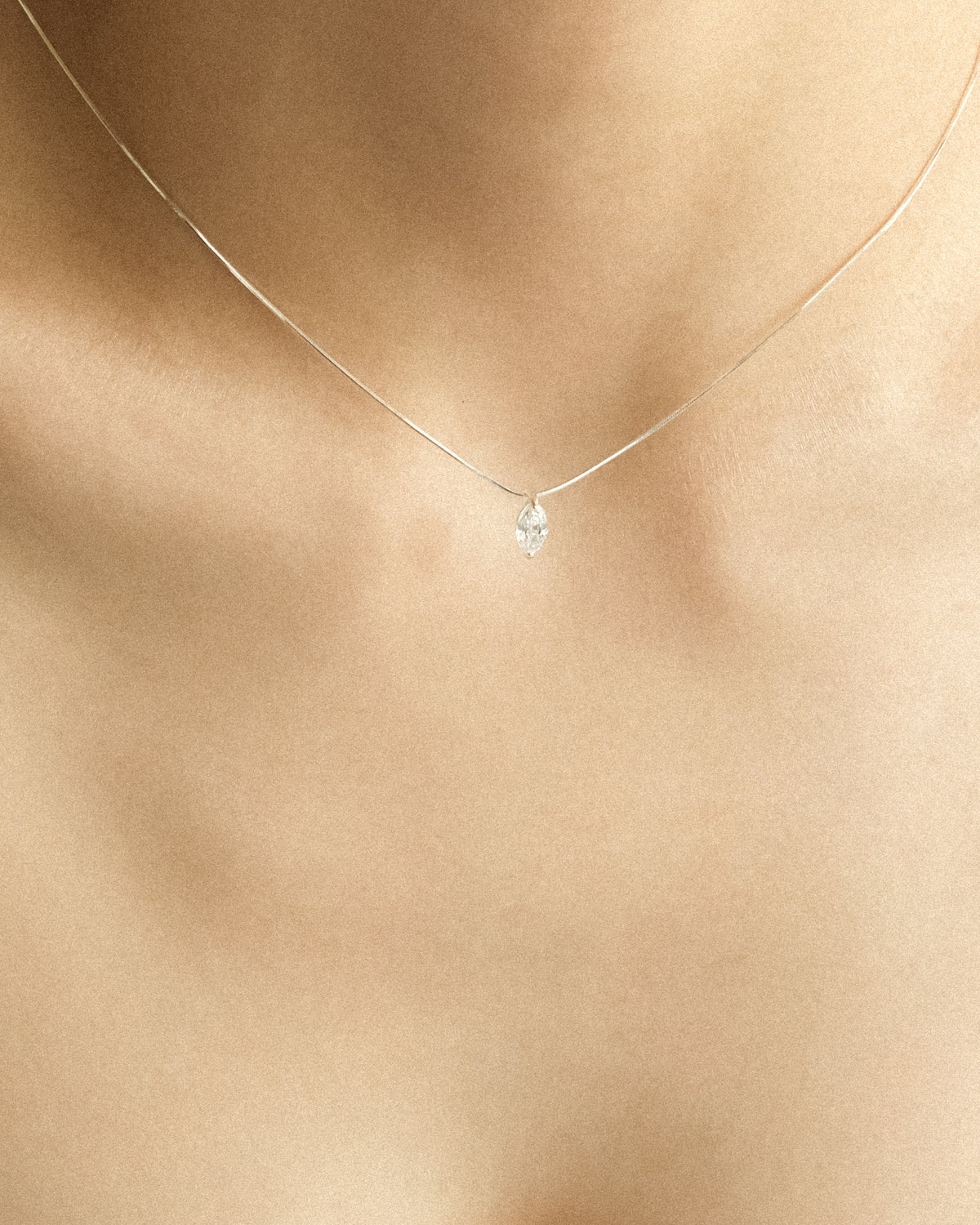 A close-up of a woman wearing a marquise diamond pendant necklace, highlighting its elegant silhouette.