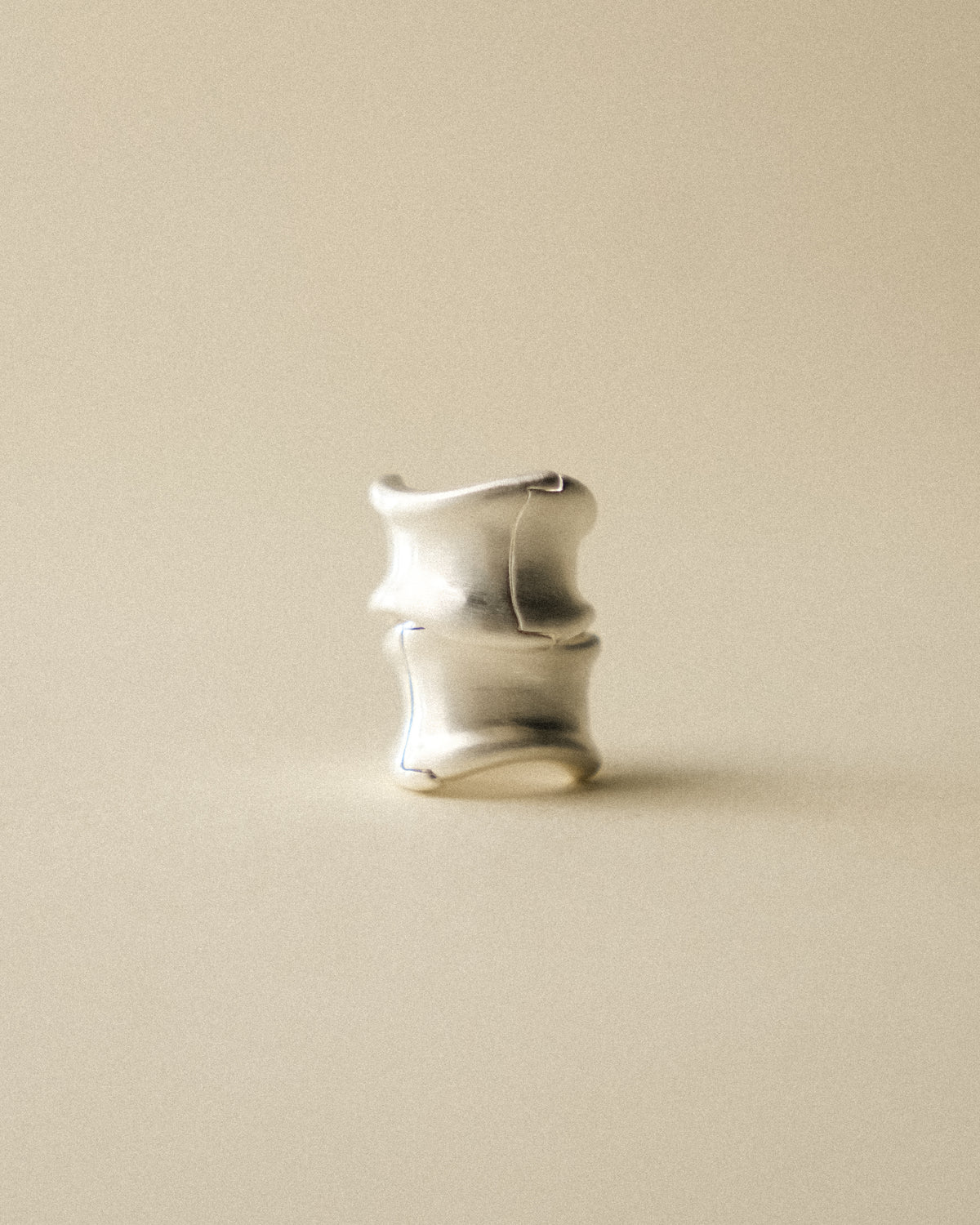 A pair of brushed curved earrings shoot against of a warm background.