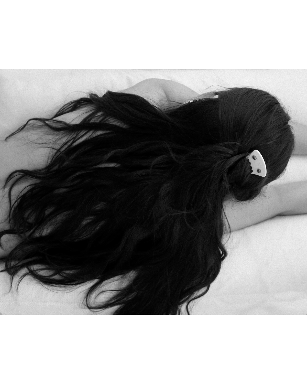 A monochrome photograph of a woman with her hair styled in a half up bun, secured with an ivory decorative hair comb featuring two malachite stones. Captured from the back against a clean white background, with soft diffused lighting that highlights the sculptural silhouette of the hairstyle, the delicate details of the hair comb, and the subtle contrast of tones in a minimal, refined composition.
